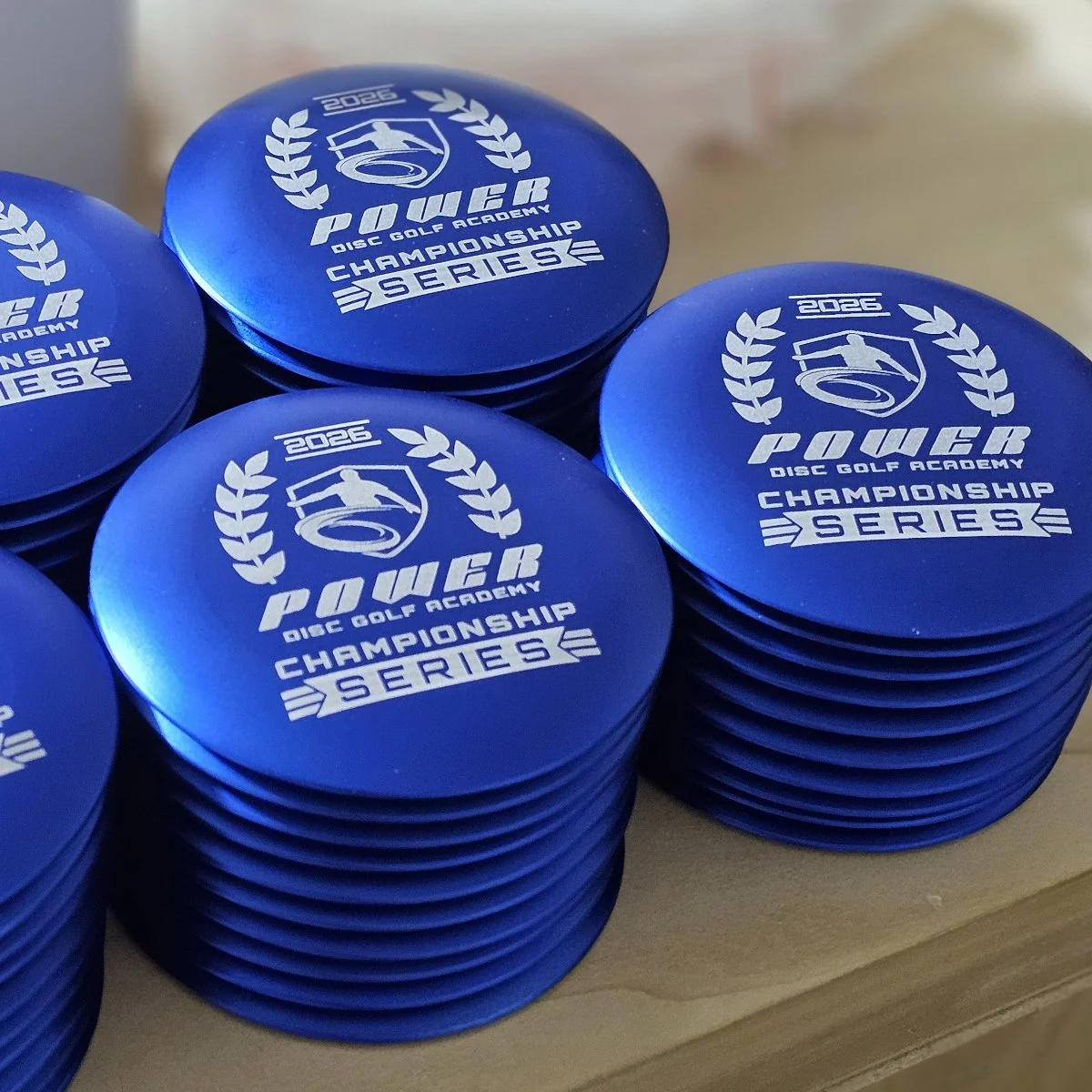 Stacks of blue metal mini markers laser-engraved for Power Disc Golf Academy Championship Series.