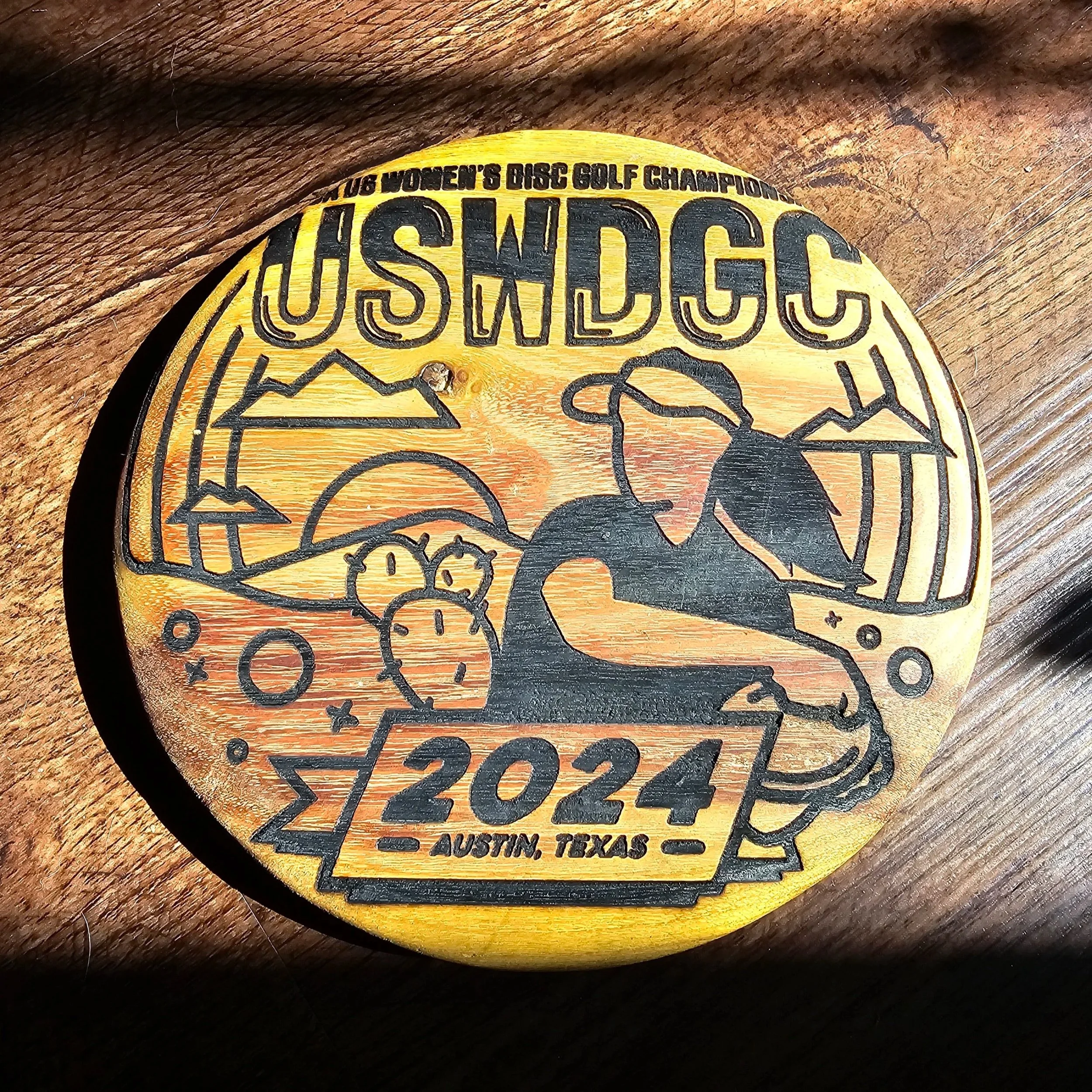Laser-engraved round wooden disc golf plaque reading USWDGC 2024 Austin, Texas with a female player throwing.