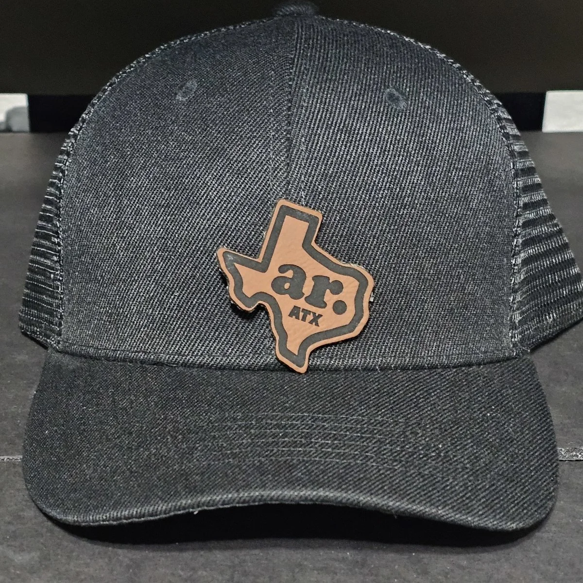 Black trucker hat with laser-engraved leatherette Texas patch for Another Round ATX.