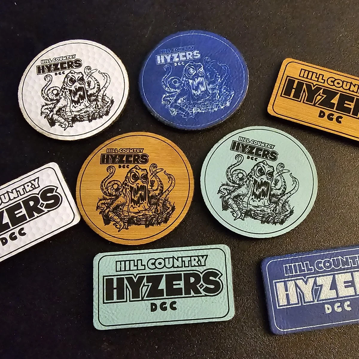 Assorted Hill Country Hyzers DGC custom patches in different colors, shapes, and materials showing mascot artwork and logo.