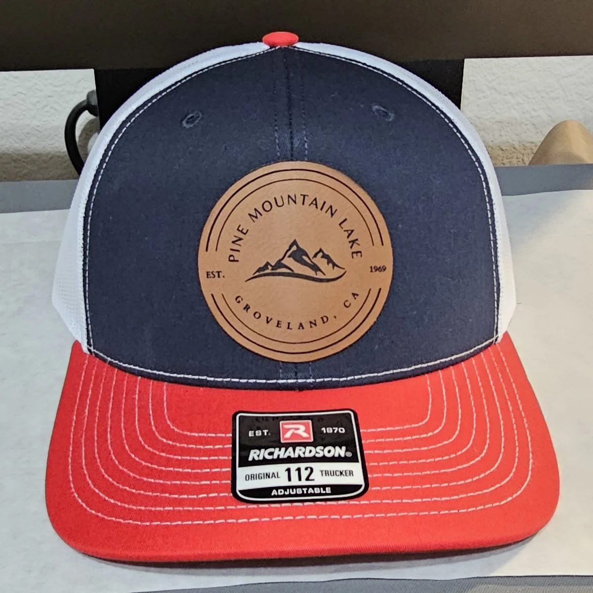 Red, white, and navy Richardson 112 trucker hat with custom round laser-engraved leatherette Pine Mountain Lake Groveland CA patch.