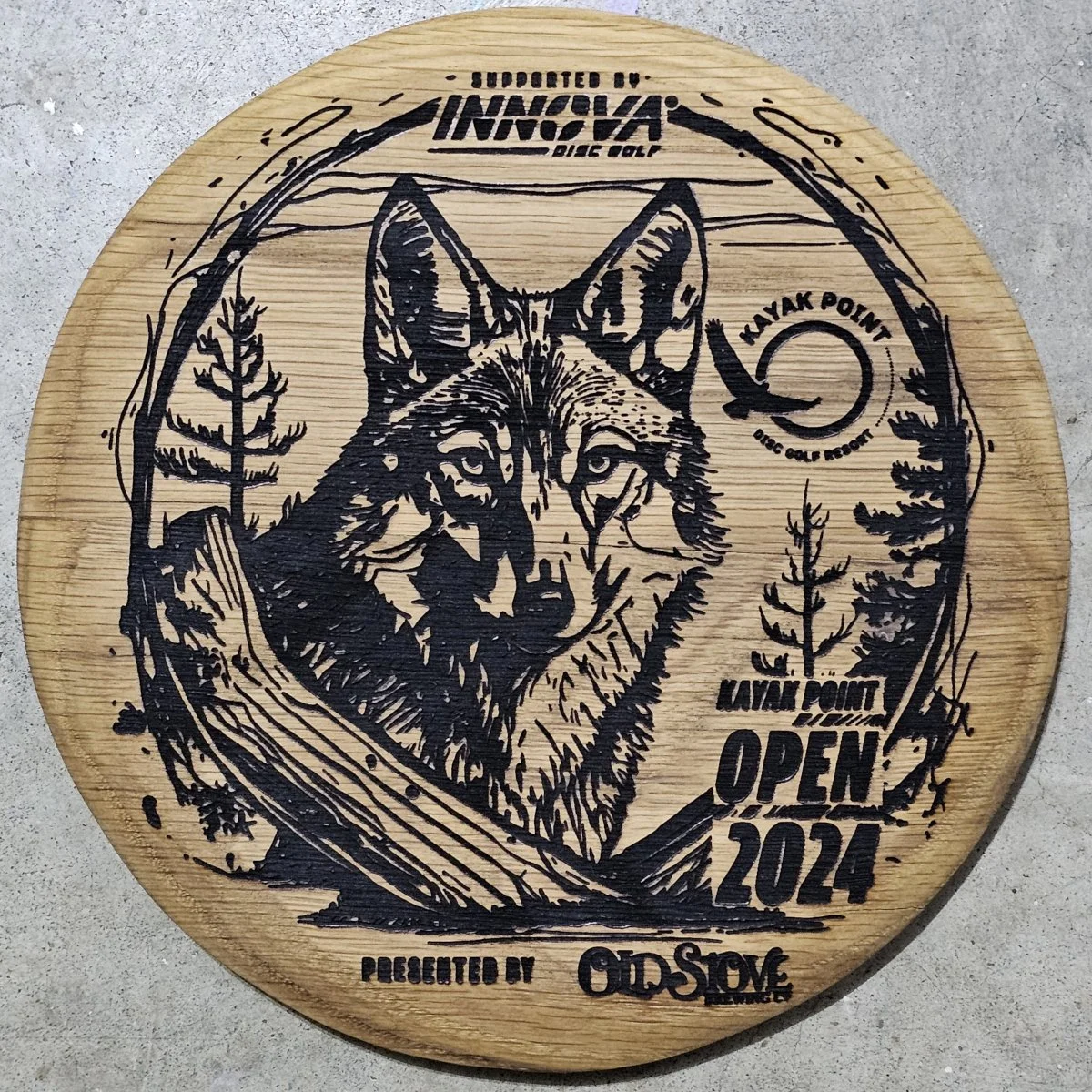 Laser-engraved oak disc golf trophy for Kayak Point Open 2024 featuring detailed wolf artwork, supported by Innova Disc Golf and Old Stove Brewing.