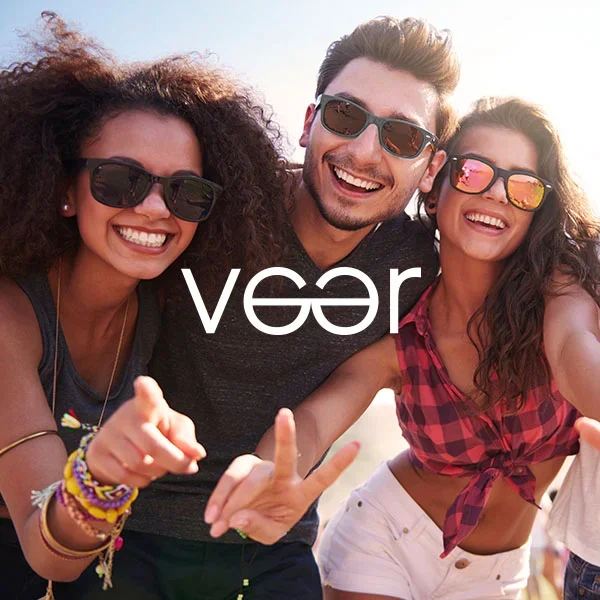 Group of three young friends smiling and taking a selfie outdoors, wearing sunglasses and casual summer clothes.