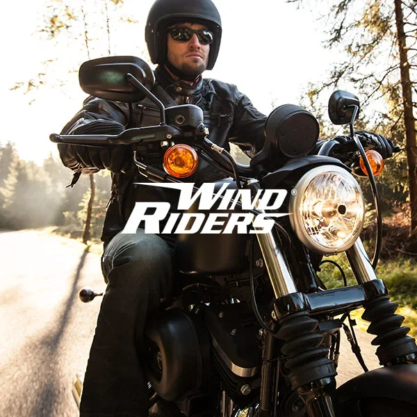 A man wearing a black helmet and sunglasses riding a black motorcycle on a forested road during sunset