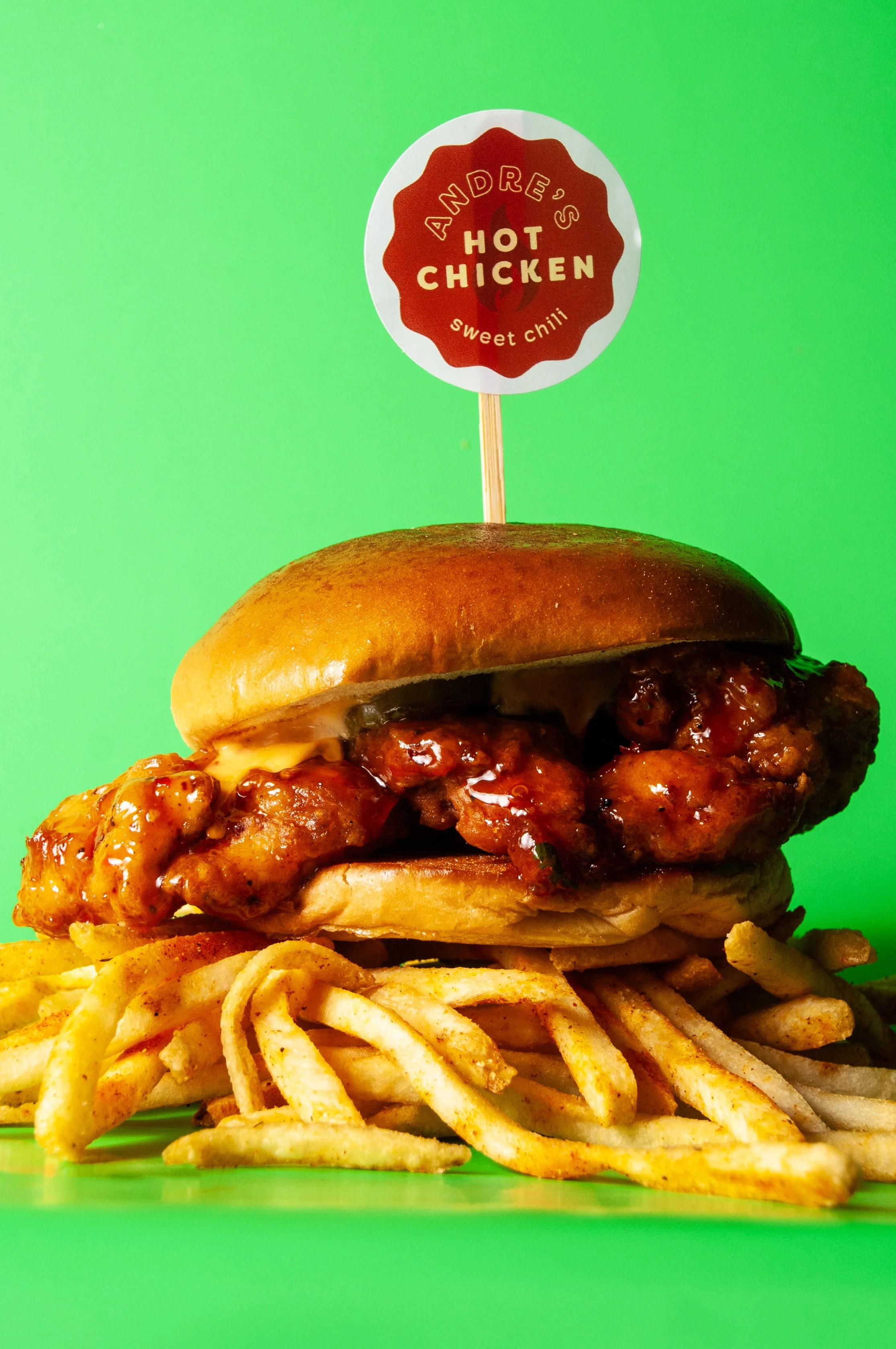 Close-up of a sticky chicken sandwich with fried chicken thigh, dipped in sweet chili sauce, dill pickles, chipotle mayo, brioche bun. choice of side.