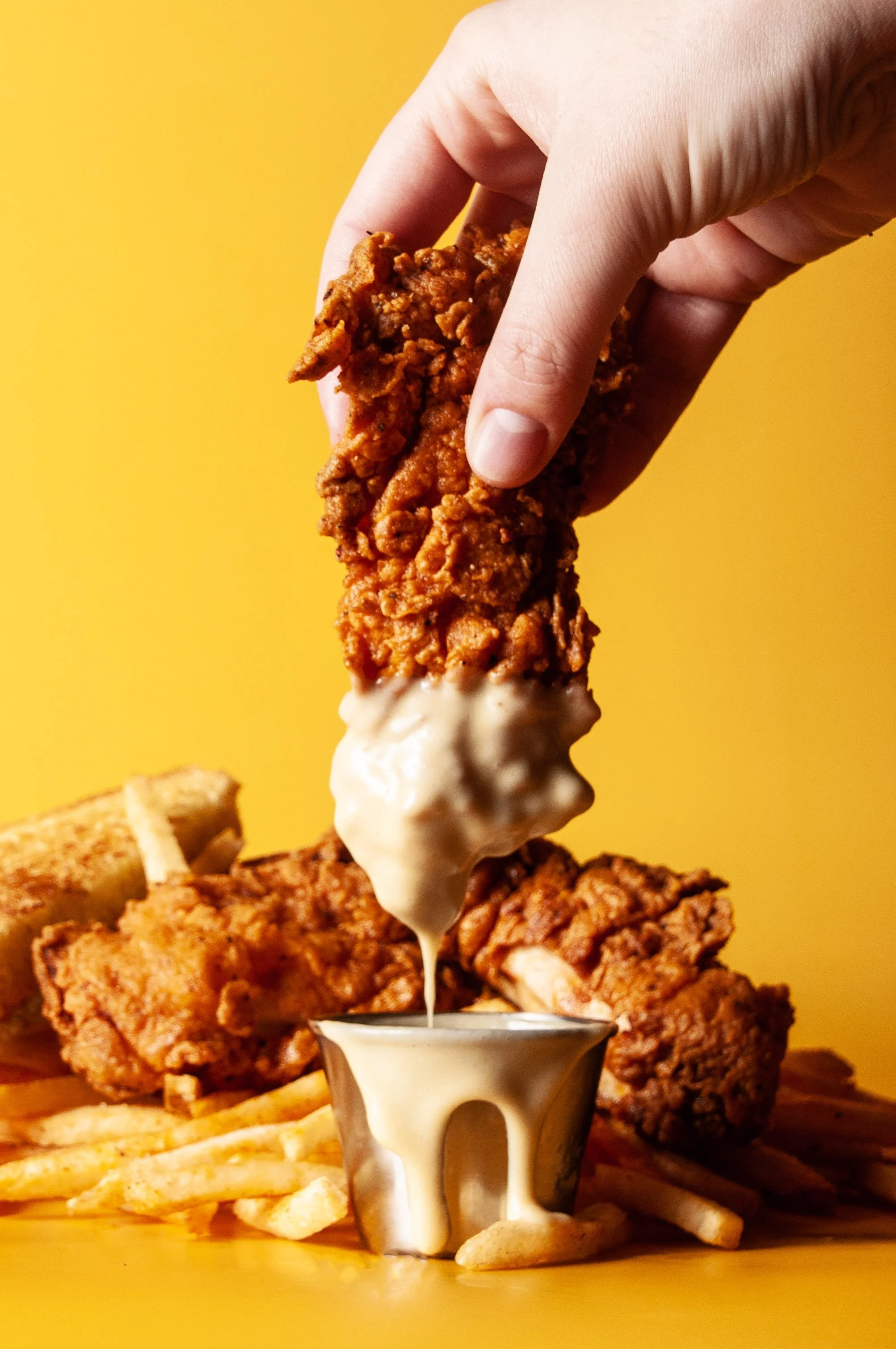 Hand dipping a classic chicken tender into sauce