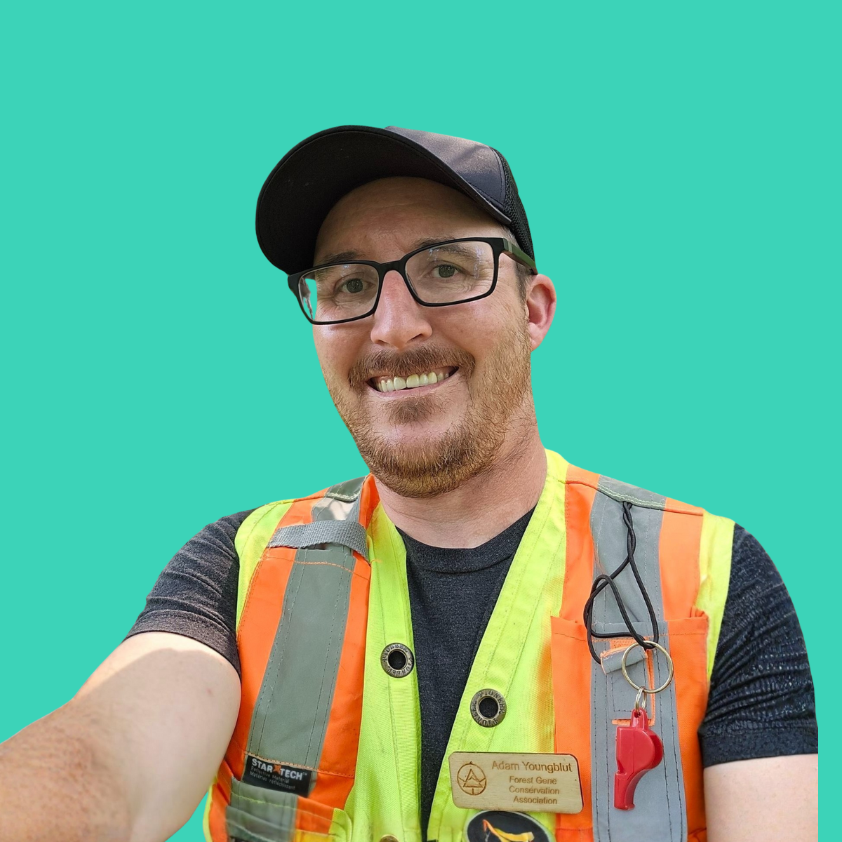 A man taking a selfie, wearing safety glasses, a black cap, a bright safety vest, and a name tag. The background is plain teal.