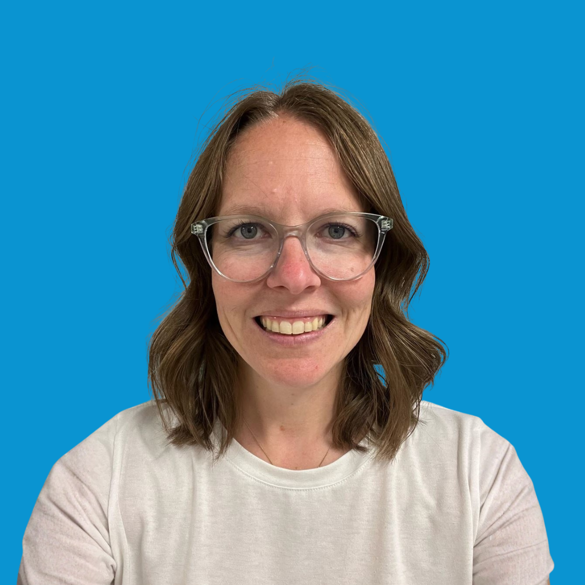 A woman with shoulder-length brown hair and glasses smiling in front of a blue background.