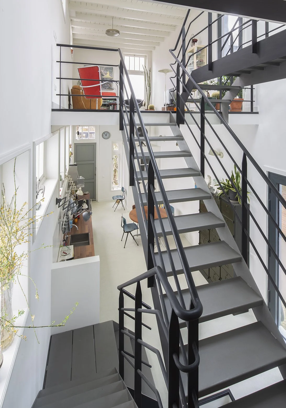 Inrichting van een moderne, ruime tweeverdiepings woning met open trap, planten en zitgedeelte op de bovenverdieping.