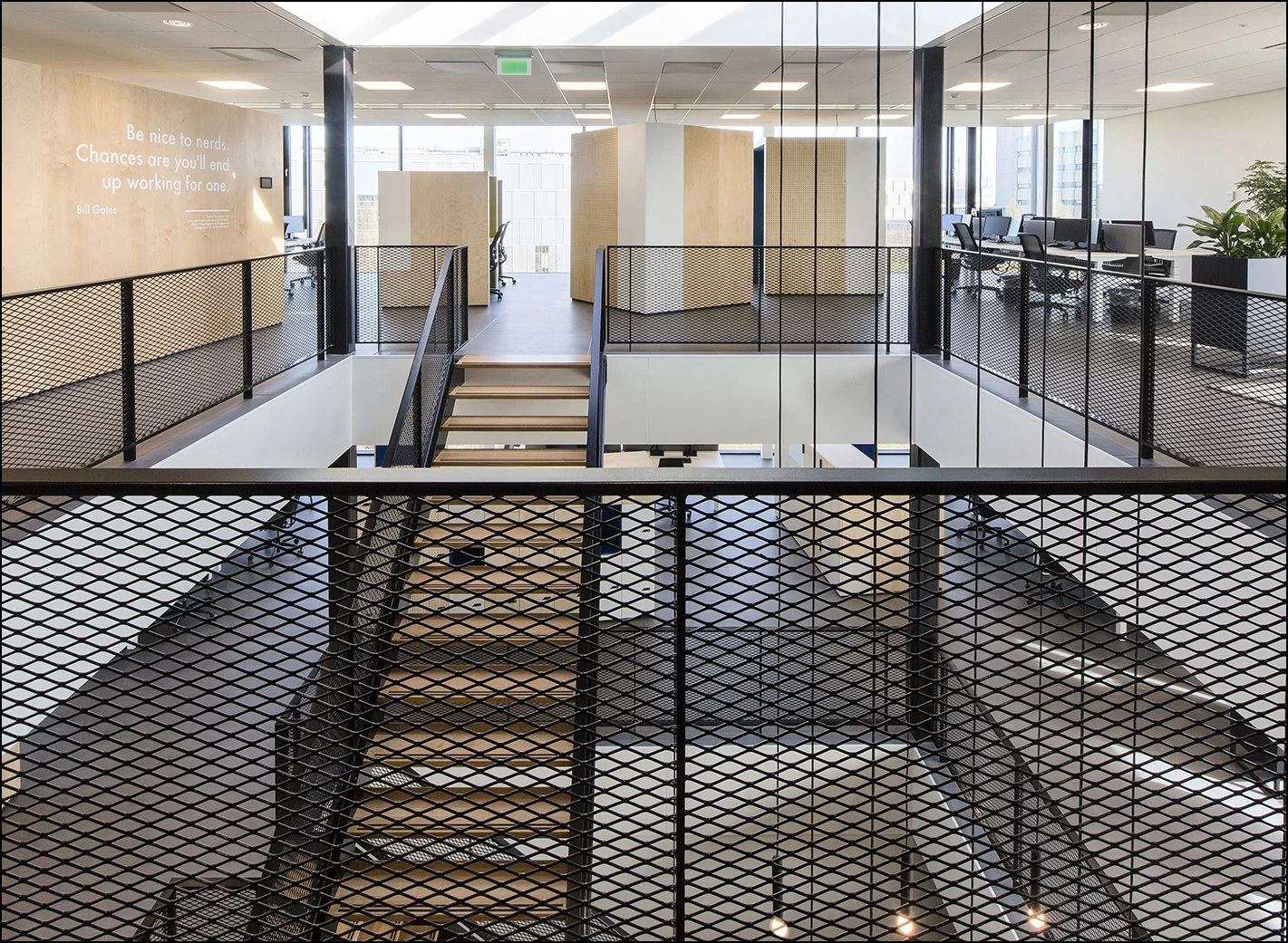 Modern kantoorruimte met open verdiepingen en trap, glazen wanden en kantoorwerkplekken met bureaus en stoelen.