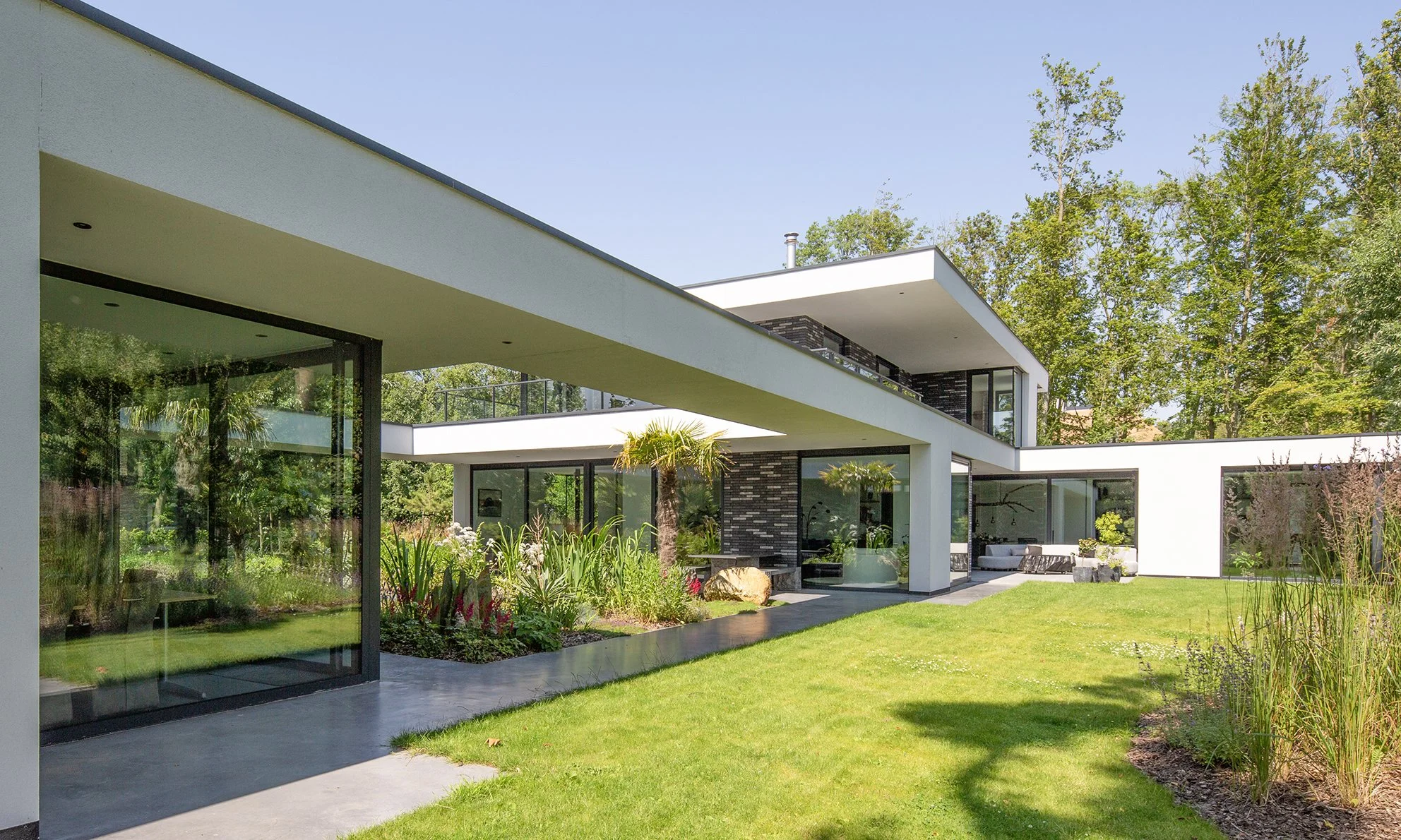 Modern wit huis met grote ramen en een tuin met gras, planten en bomen.