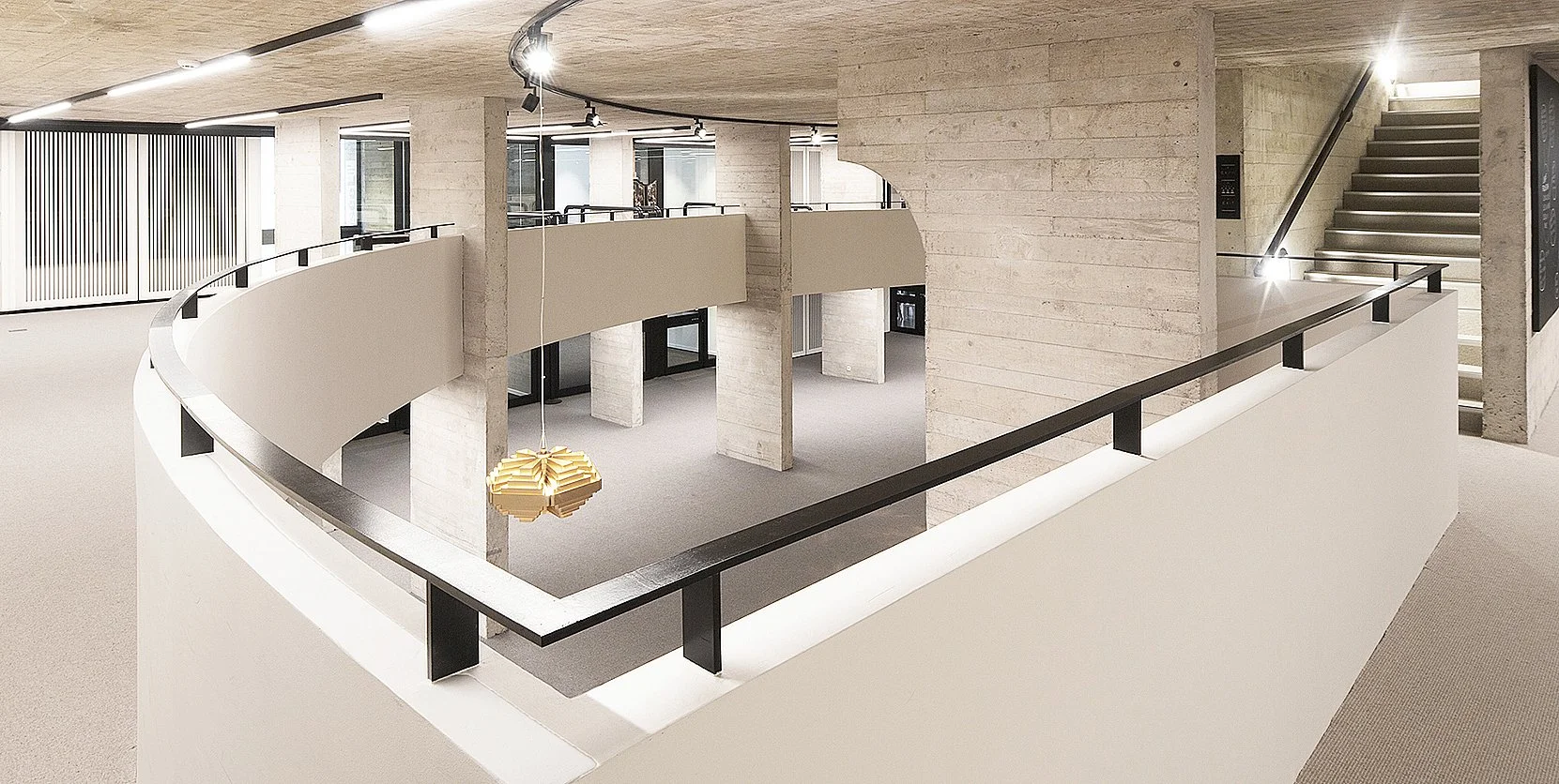 Interieur van een modern gebouw met ronde balkonranden, trap, verlichting en een opvallende hanglamp.