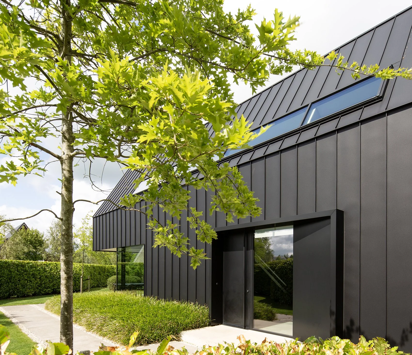 Een modern zwart metalen huis met grote ramen, omgeven door groene bomen en struiken.