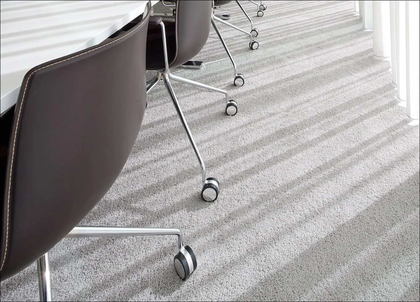 Kantoor met bureaustoelen en een witte tafel, vloerbedekking met strepenpatroon.