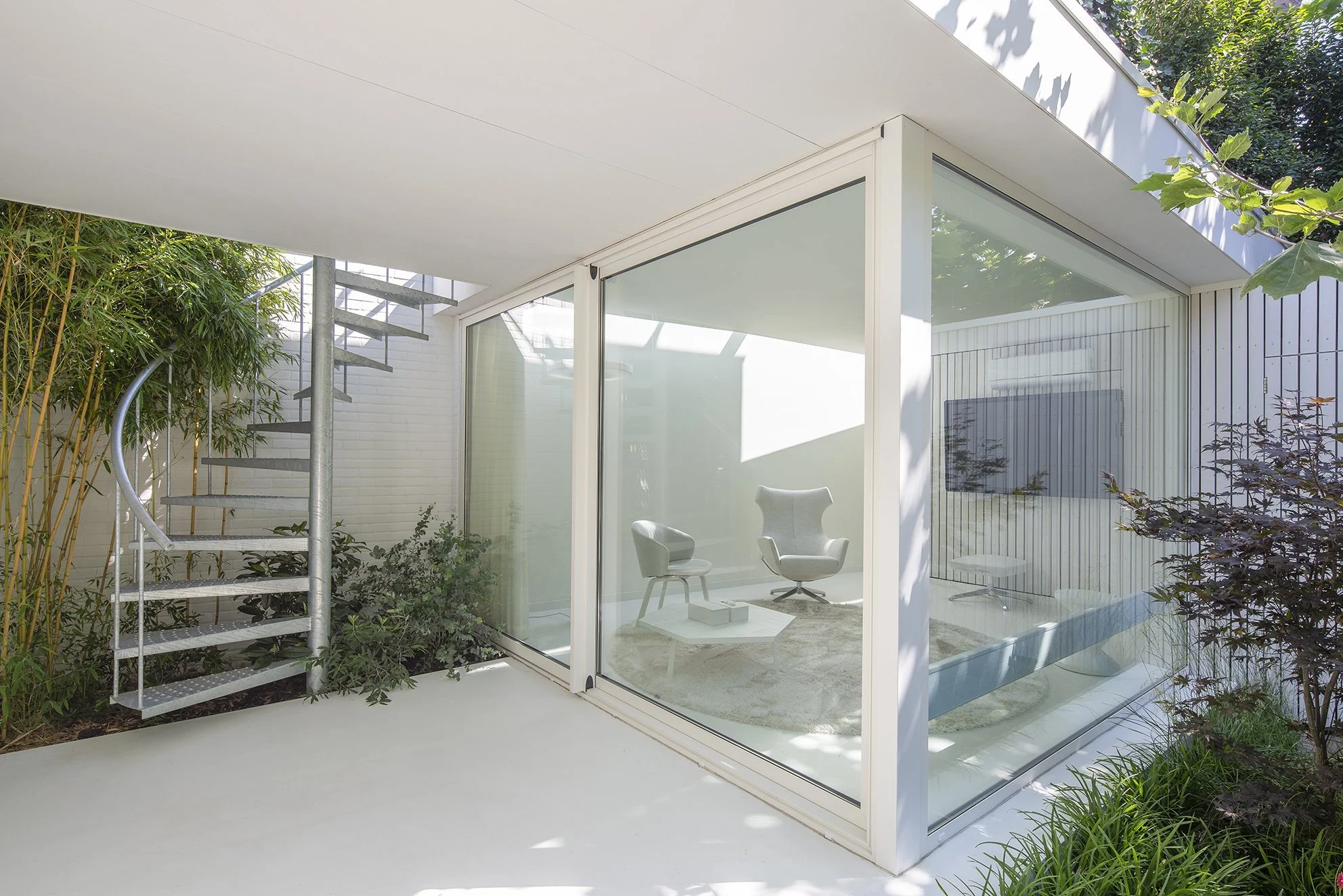 Moderne veranda met grote glazen schuifdeuren, omgeven door groene planten en een tuin.