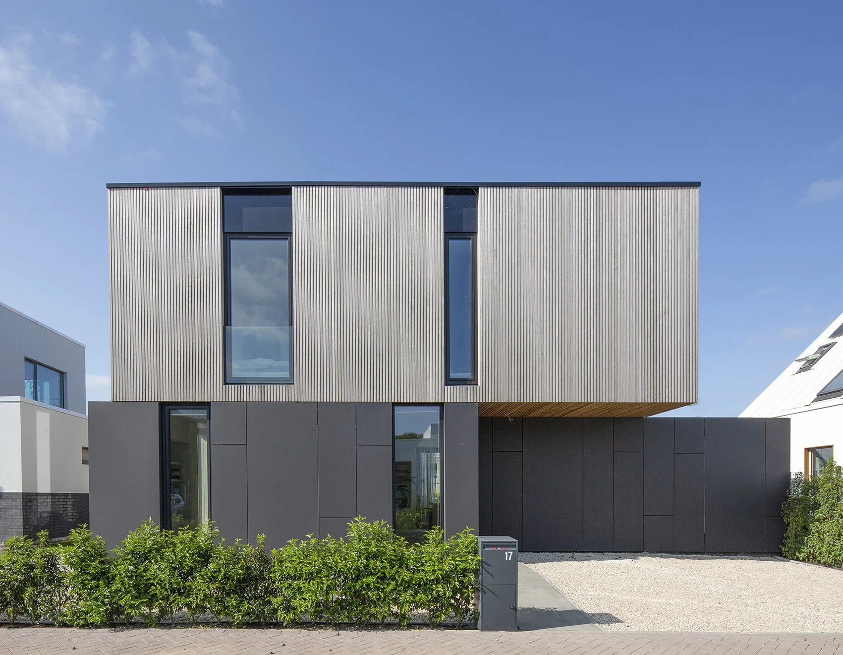 Moderne woning met glazen ramen en houten gevelbekleding, met een tuin en een oprit voor de woning.