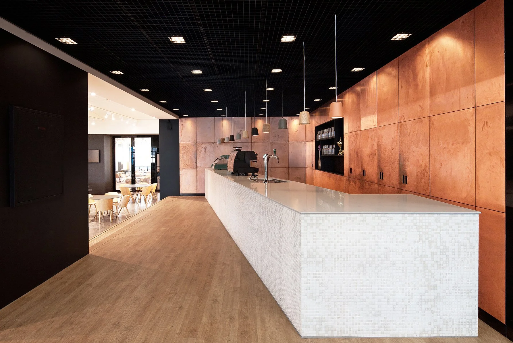 Moderne cafébar met witte toog, houten vloer, zwart plafond en isolerende houten wand met open vakken met glazen en decoraties.