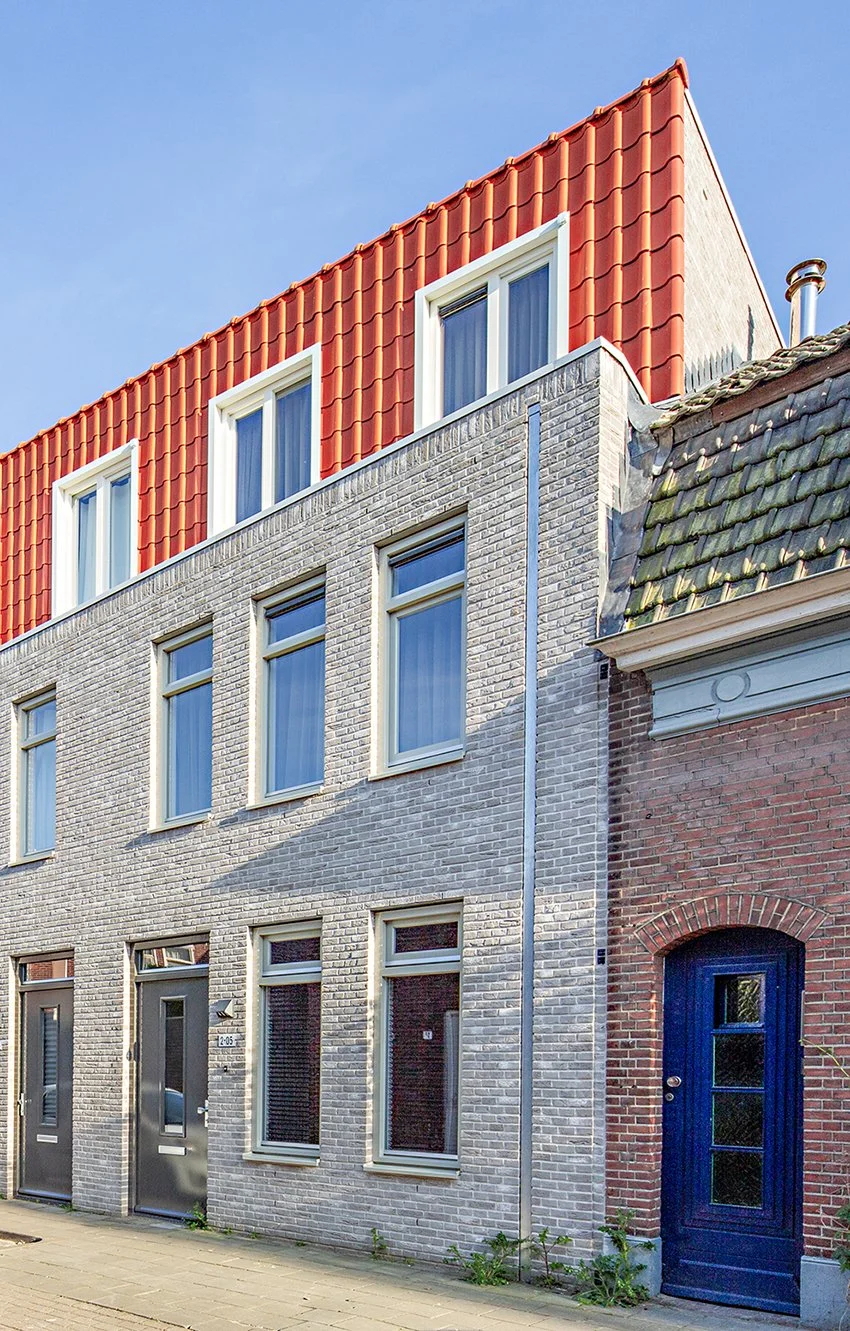 Drie gelijksoortige witte bakstenen huizen met grote ramen en donkere deuren, met een rood en hellend dak en blauwe hemel op de achtergrond.