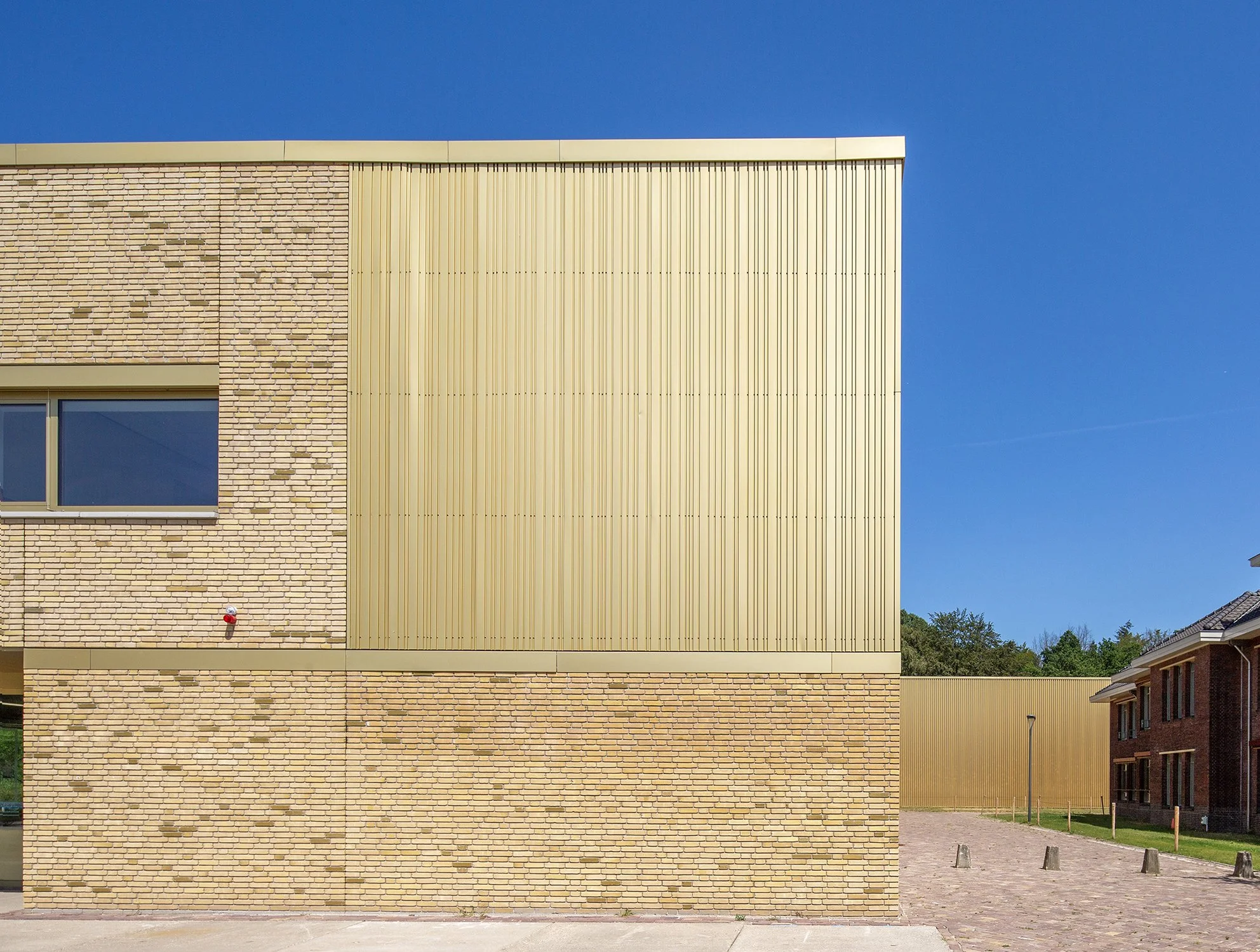 Een modern gebouw met een gevel van geel baksteen en verticale aluminiumpanelen tegen een heldere blauwe lucht gefotografeerd door architectuurfotograaf John van Groenedaal