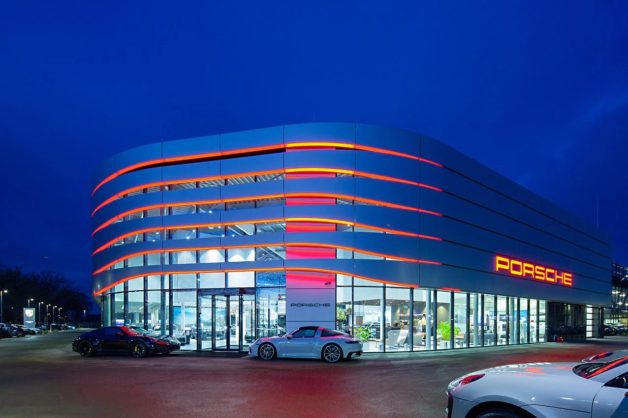 Moderne Porsche dealer met glazen gevel en neonverlichting in de avond.