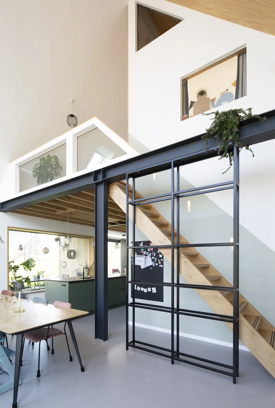 Interieur van een modern, open woonhuis met een open trap, grote ramen, en een keuken en eethoek.