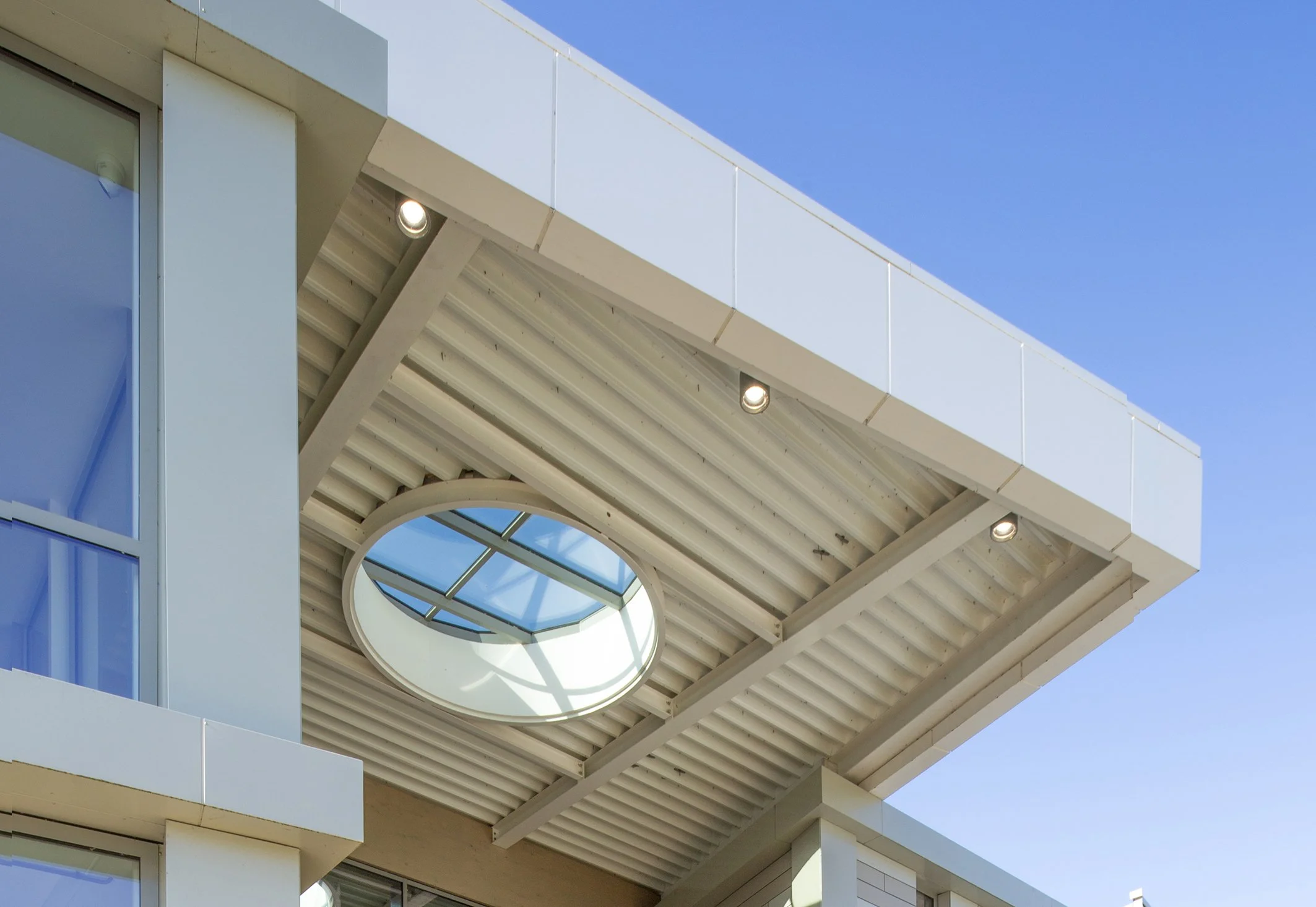 Modern gebouw met grote ramen, witte en blauwe gevel en een balkon met glazen rand onder een heldere blauwe hemel.