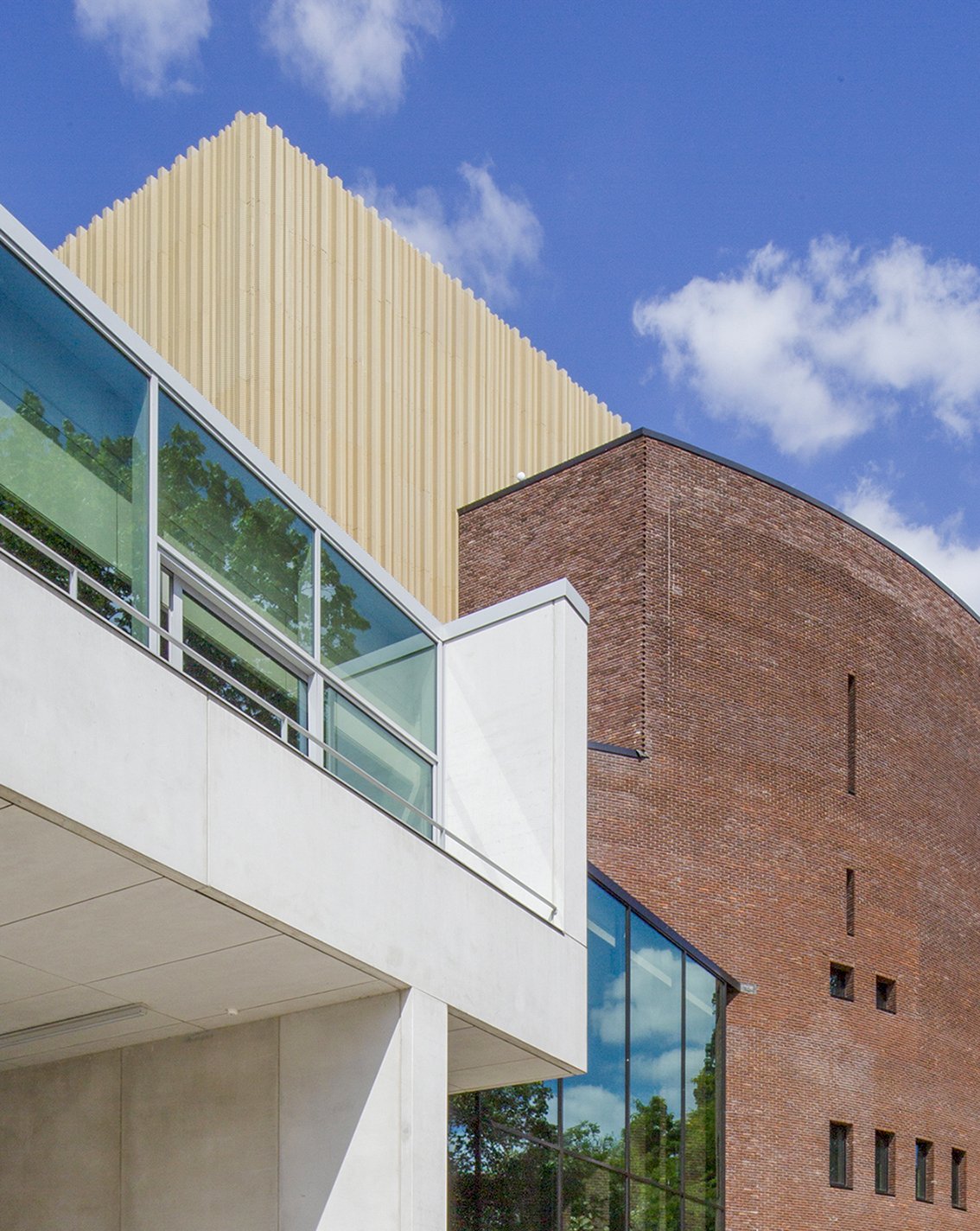 Modern gebouw met grote ramen, een rood bakstenen muur en een houten gevel onder een blauwe hemel met wolken.