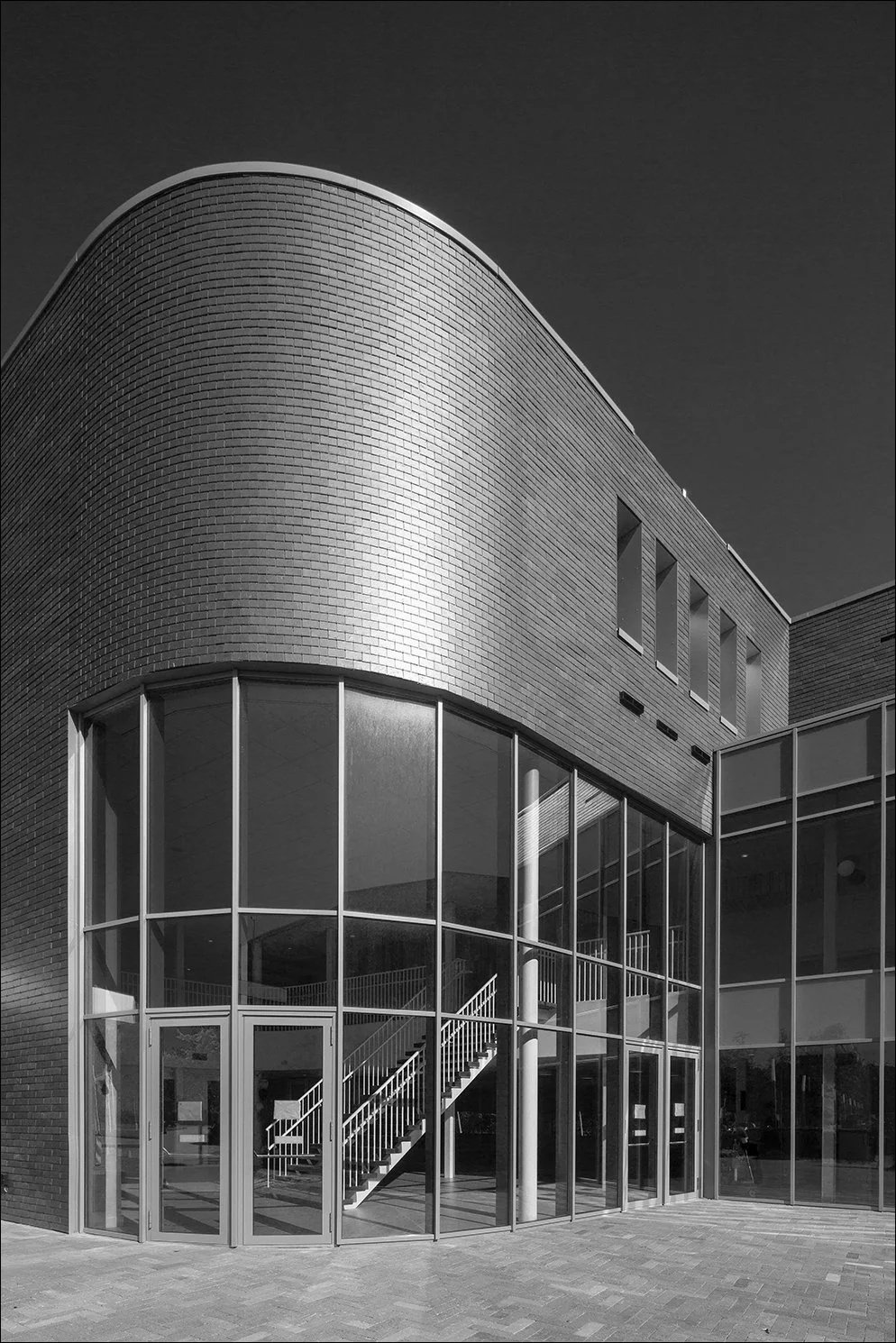 Modern gebouw met ronde hoek en grote glasramen, zwart-wit foto.