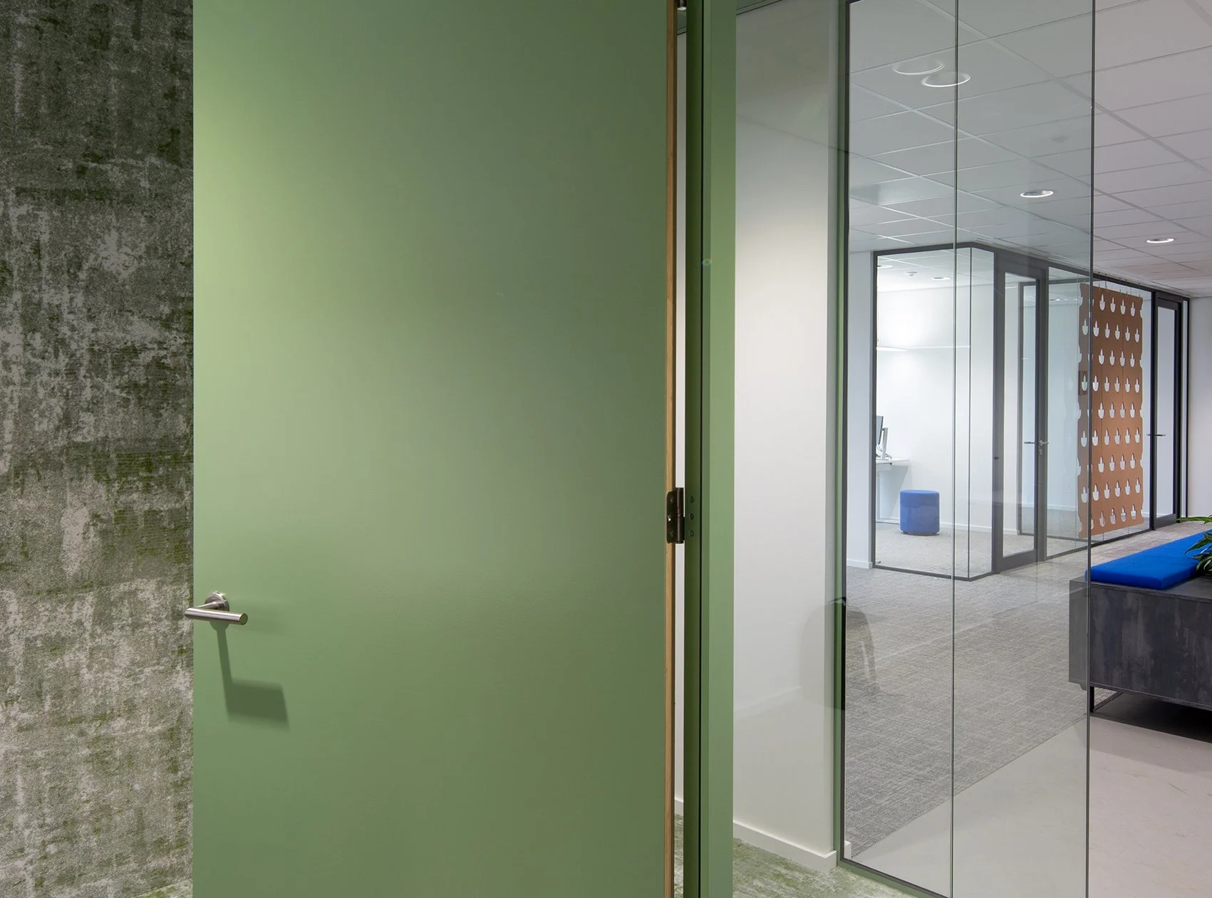 Kantoordeur die openstaat, met een groen paneel en glastype muren binnen een modern kantoor.