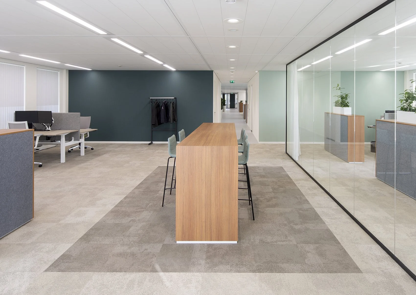 Kantoorruimte met vergadertafel, stoelen, werkplekken, en planten, gescheiden door glazen wanden.