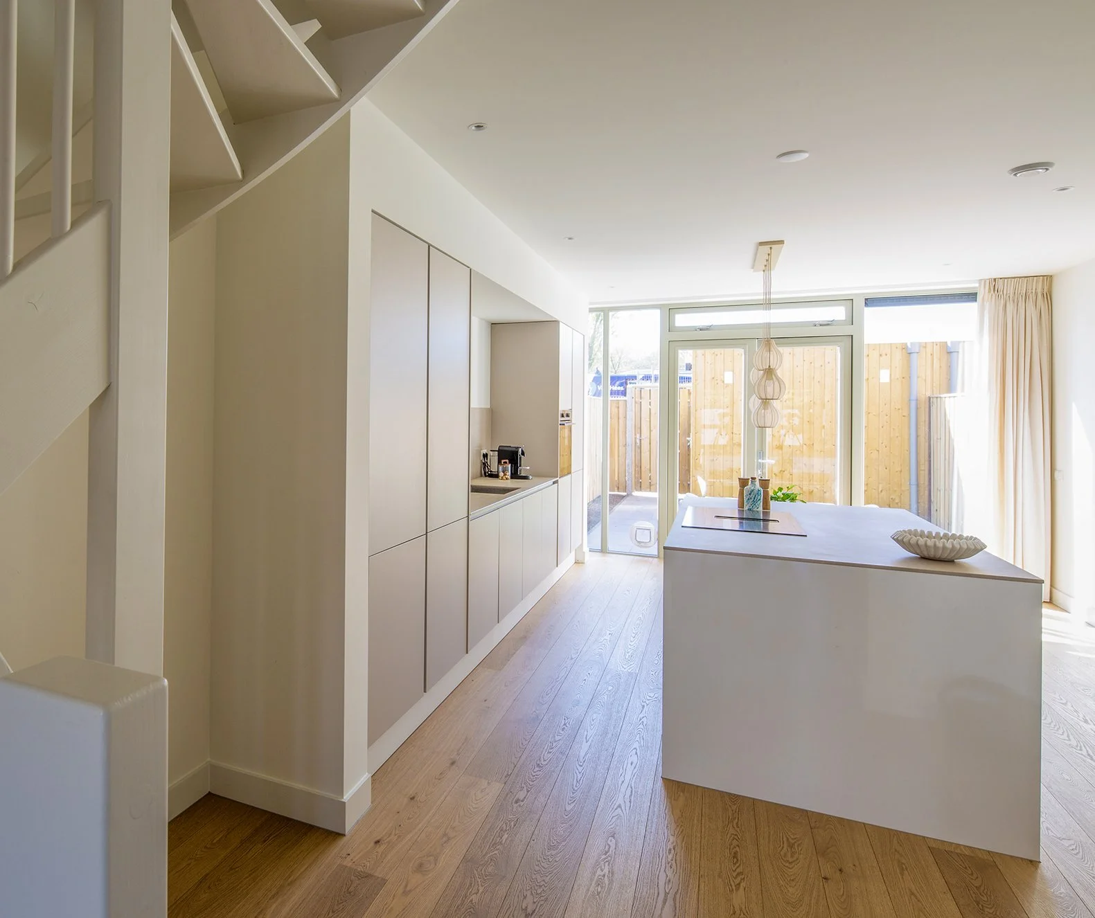 Een moderne, lichte keuken met een eethoek, grote ramen, een houten vloer en een centraal eiland.