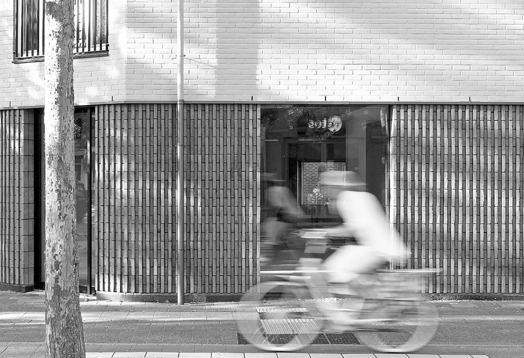 Bevroren straat met een boom, een raam met houten panelen, en een fietser die snel voorbij rijdt, vastgelegd in zwart-wz