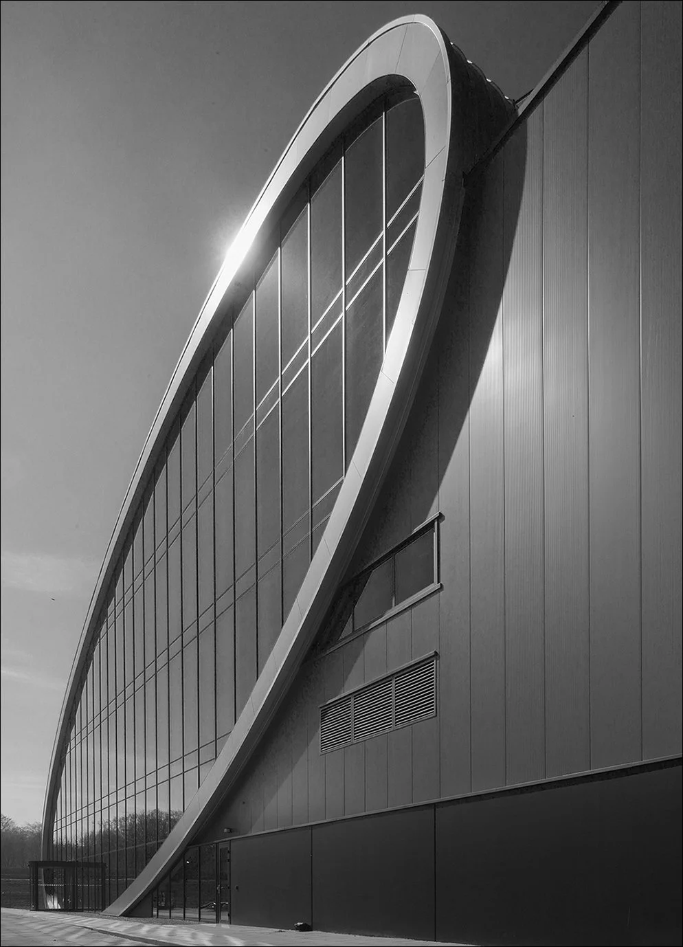 Moderne architectuur met een grote glazen gevel en een opvallende ronde vorm, zwart-wit foto.