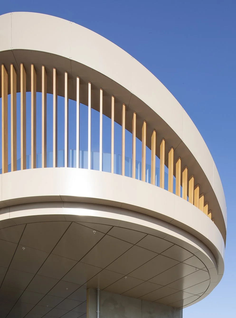 Een moderne witte ronde bouw met houten en glazen balustrades onder een heldere blauwe hemel.