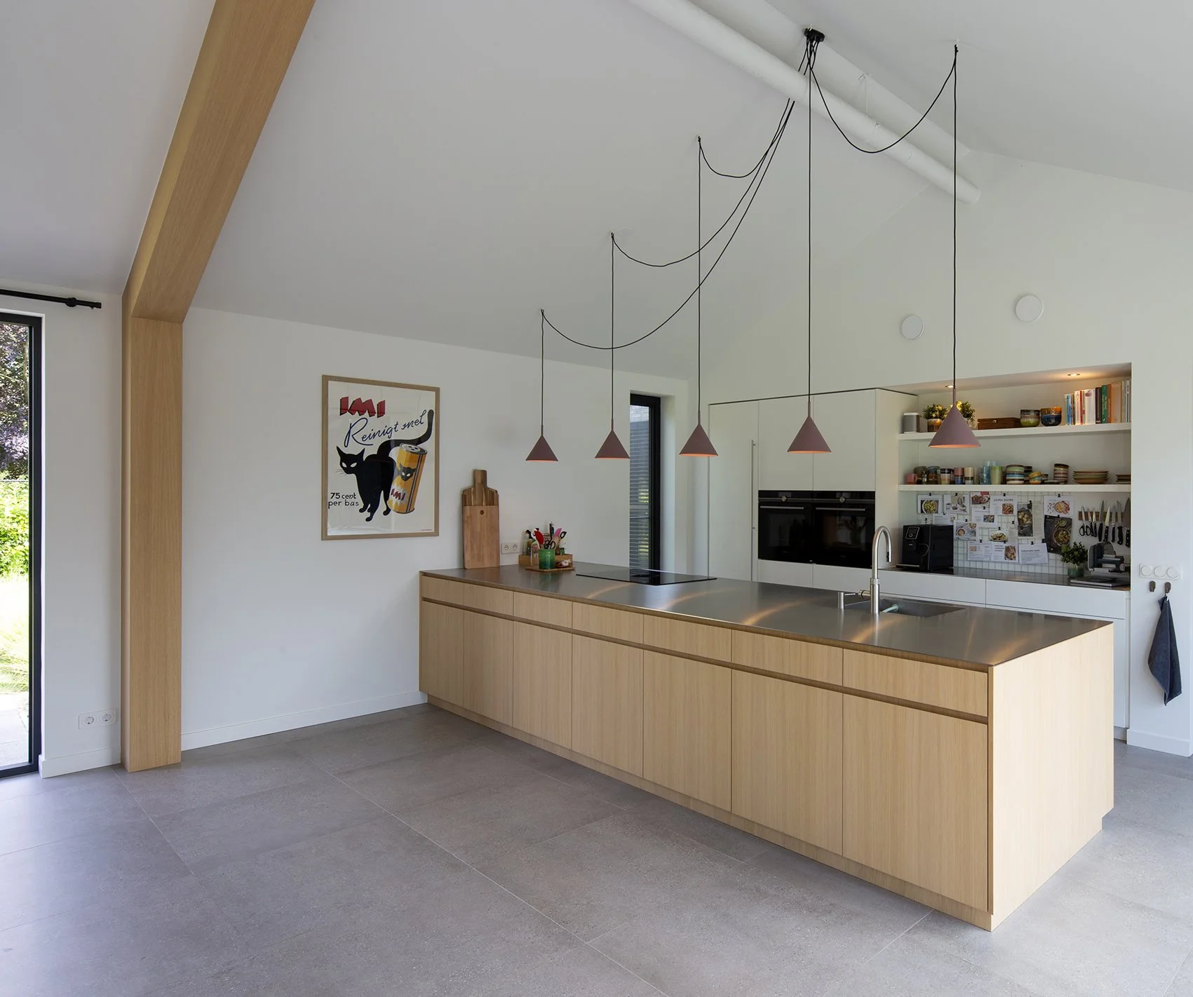 Moderne keuken met een houten eiland, een muurrek met kruiden en bestek, en een poster met een kat en een drankje, lichte muren en grote ramen.