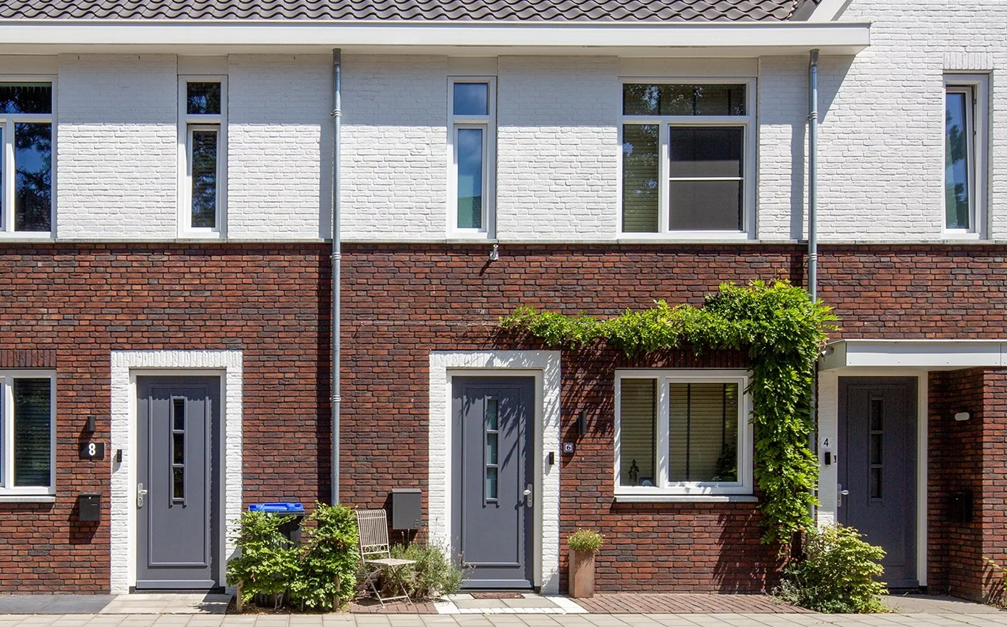Rij woningen met rode bakstenen gevels, witte kozijnen en grijze deuren, met groen begroeide gevel en planten voor de ingang gefotografeerd door architectuurfotograaf John van Groenedaal.