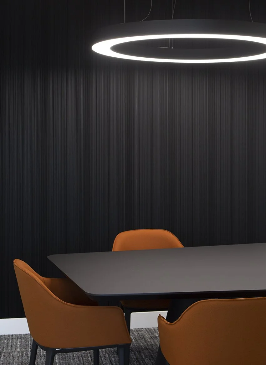Moderne vergaderzaal met zwart tafel, oranje stoelen en een grote ronde plafondlamp.