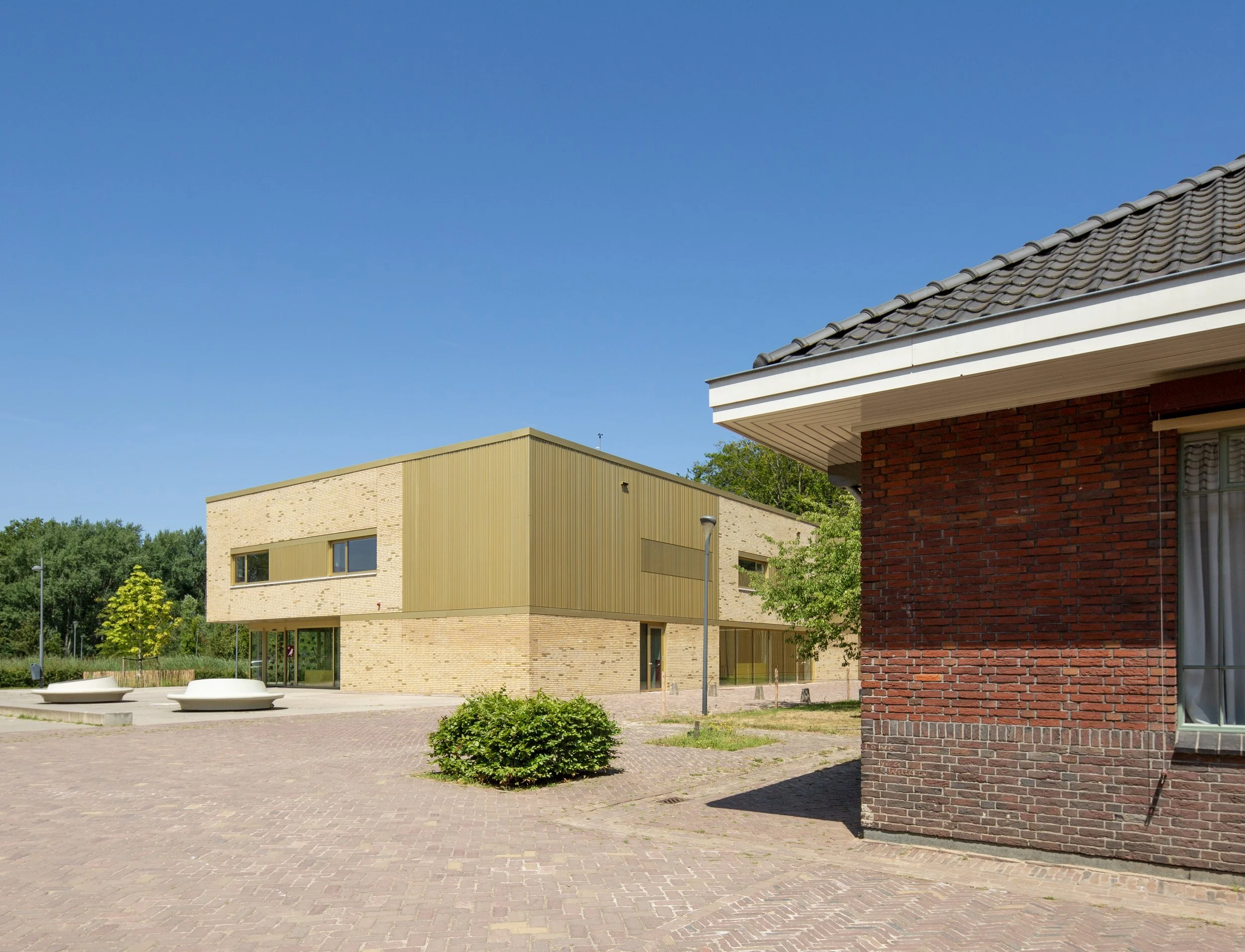 Moderne gebouwen met verschillende gevelmaterialen en een stenen plein met enkele planten en zitbanken onder een blauwe lucht gefotografeerd door architectuurfotograaf John van Groenedaal.