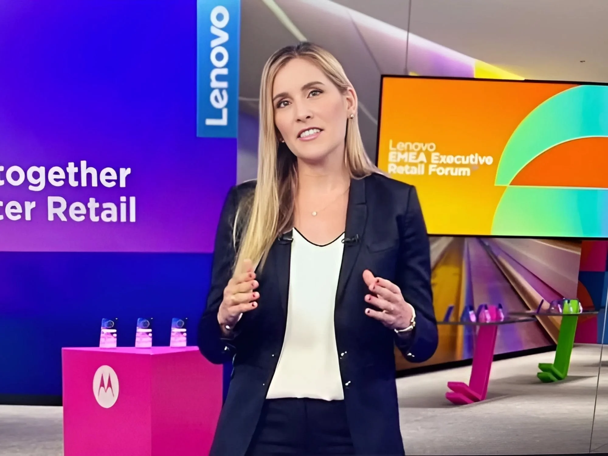 Une femme en tenue professionnelle s'exprimant lors d'une conférence sur le commerce de détail, avec derrière elle une affiche colorée sur laquelle on peut lire « Together for Retail » (Ensemble pour le commerce de détail) et « Lenovo EMEA Executive Retail Forum » (Forum exécutif Lenovo EMEA sur le commerce de détail).