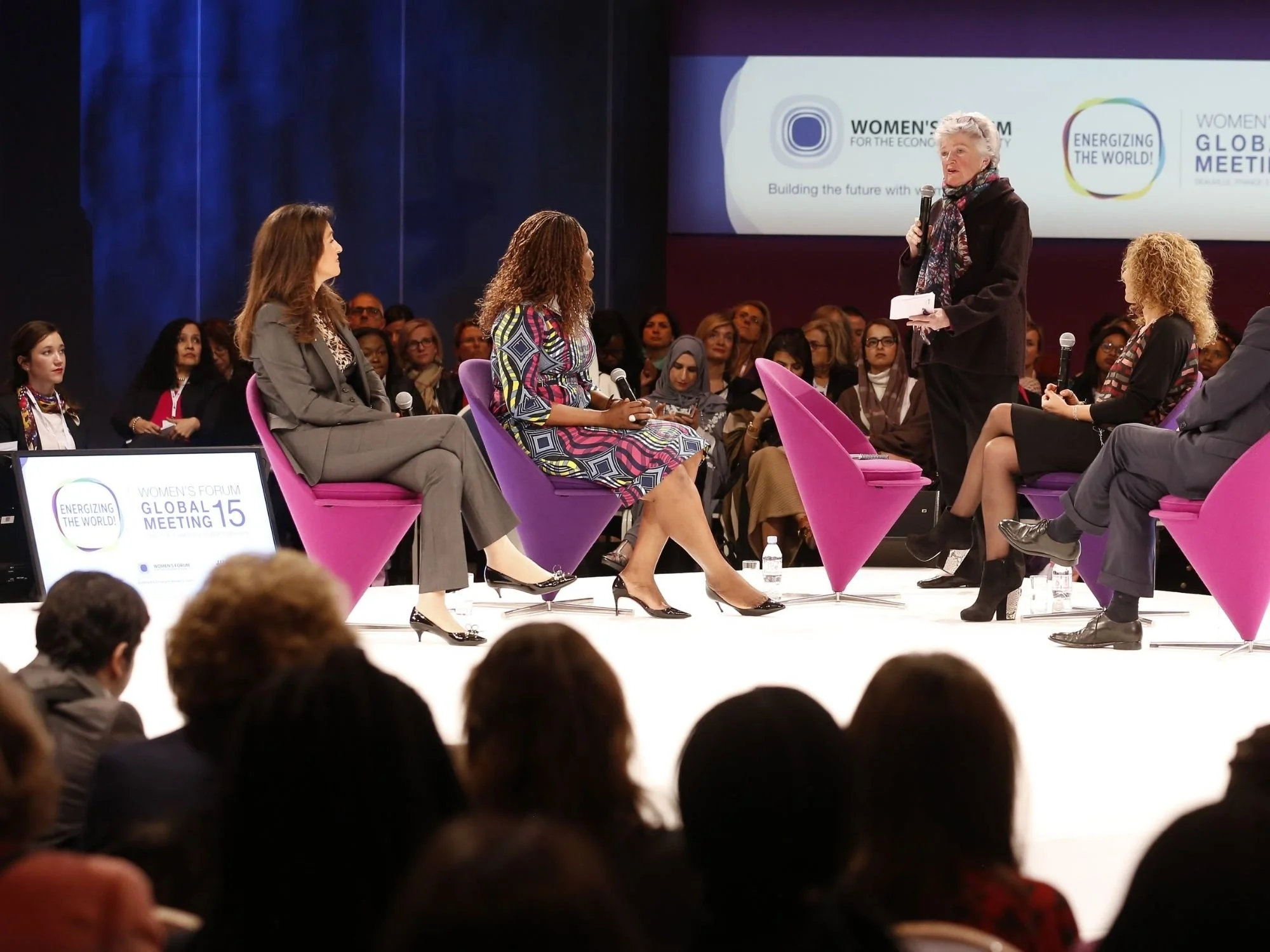 Table ronde du forum des femmes lors de la réunion mondiale 15, avec plusieurs femmes assises sur scène et une femme debout parlant au micro, sous le regard du public.
