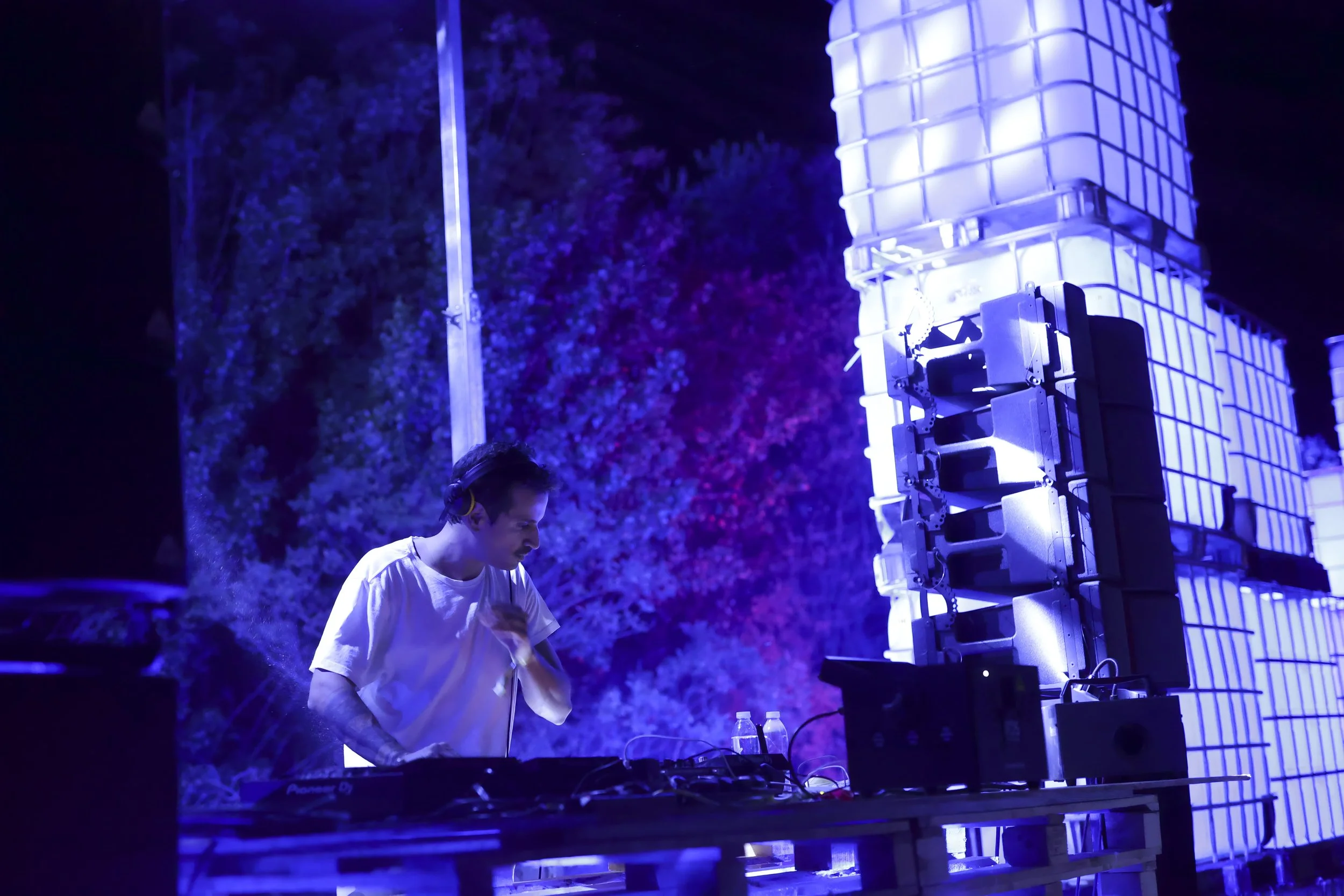 Woman painting on a large beige canvas at night, with art supplies on a small table nearby.