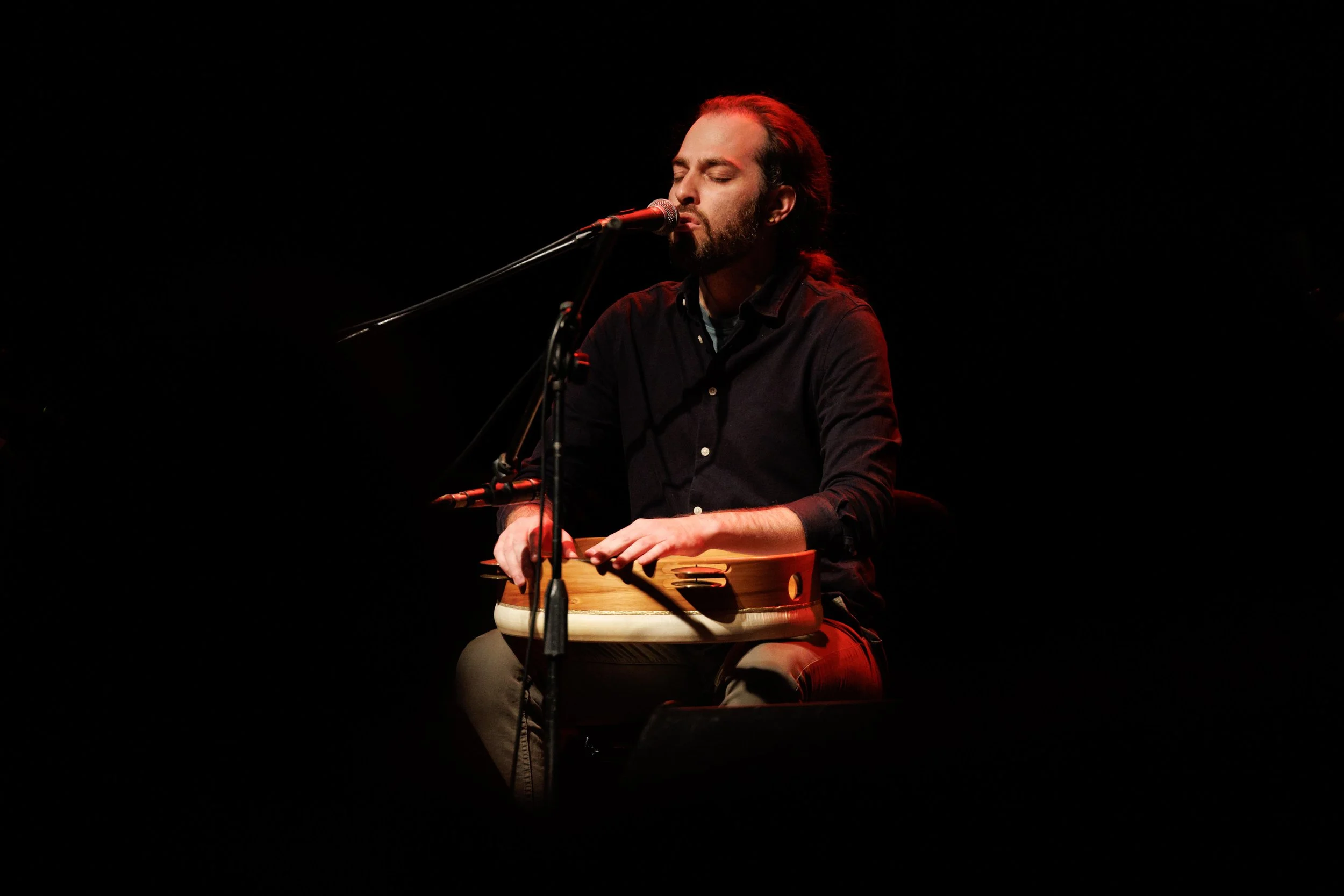 A man in a black t-shirt standing against a wall with blue and red lighting.