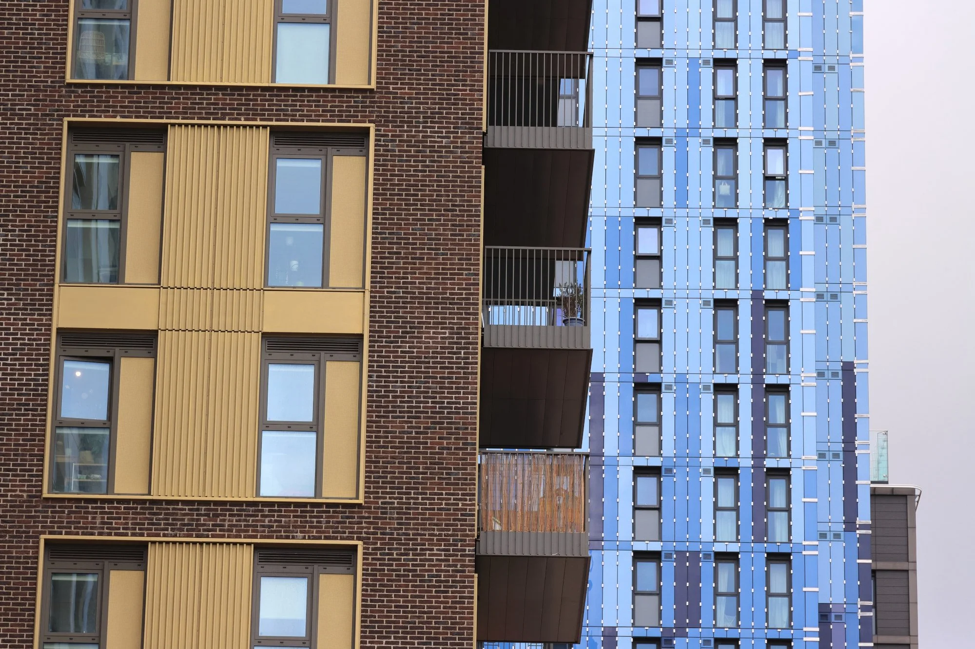 A volcanic landscape with colorful, smooth rocks in shades of brown, orange, and yellow in the foreground, and snow-capped mountains and a glacier in the background under a cloudy sky.
