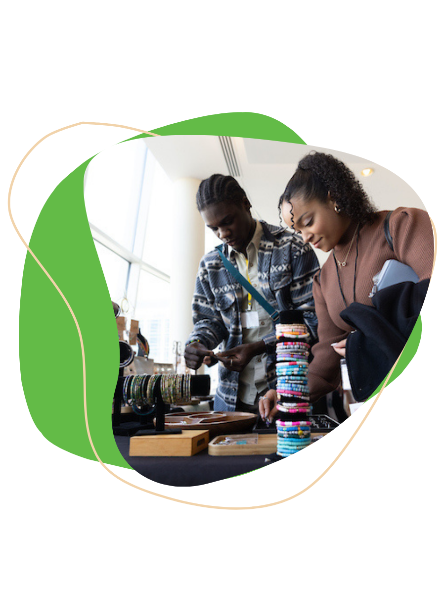 Two women browsing jewelry and fabric items at a market or craft fair.