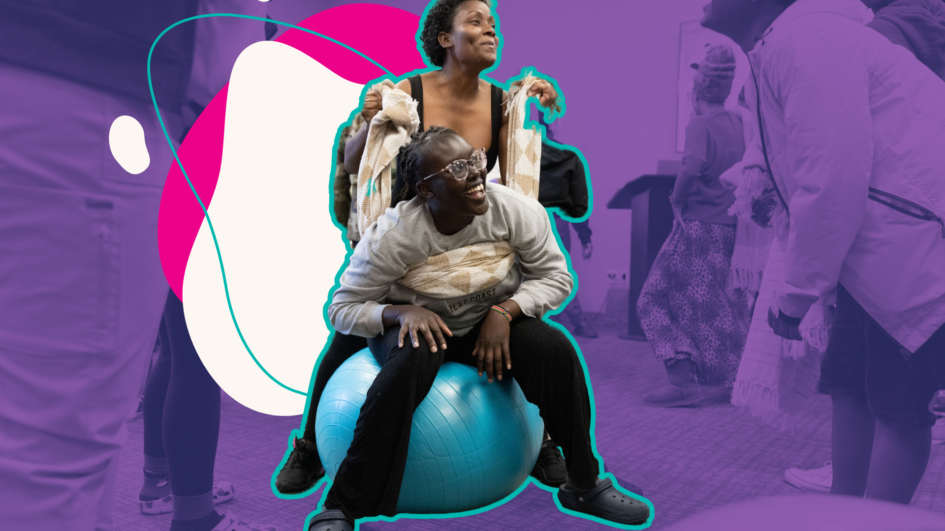 Two women laughing, one sitting on a blue exercise ball and the other standing behind her, in a group activity with others in the background.