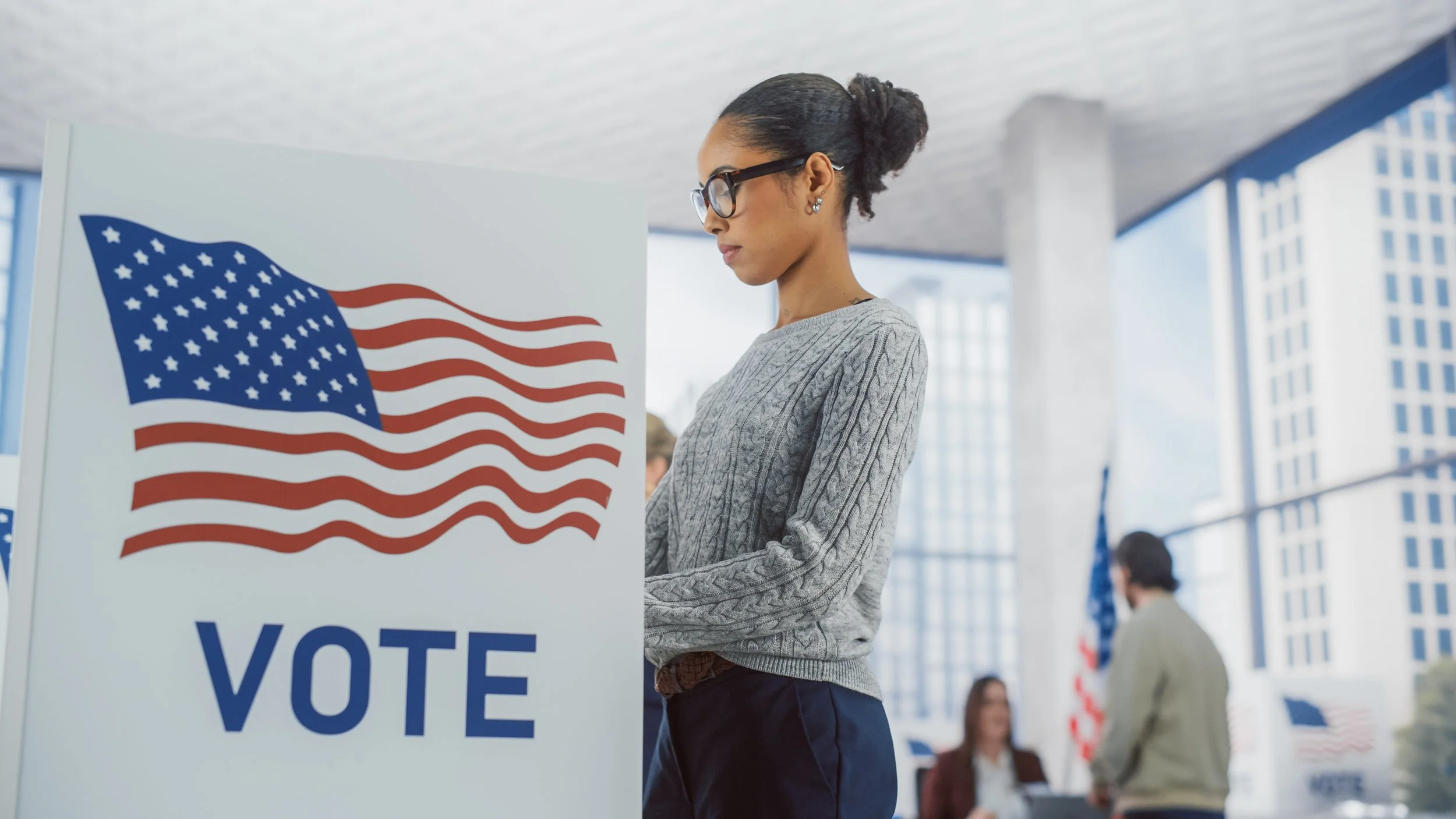 Woman voting at a polling station with an American flag and a 'VOTE' sign