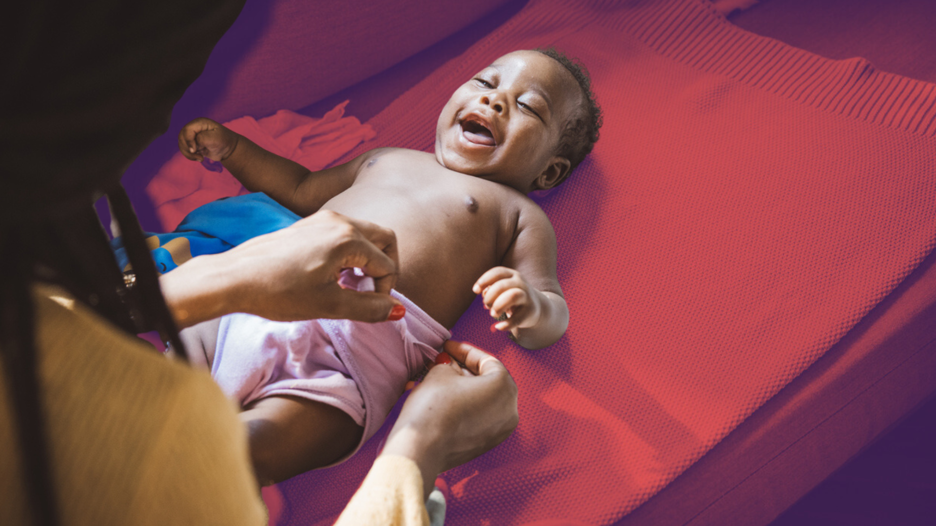 A young child lying down is being held by a mother. The child is laughing and appears to be happy.