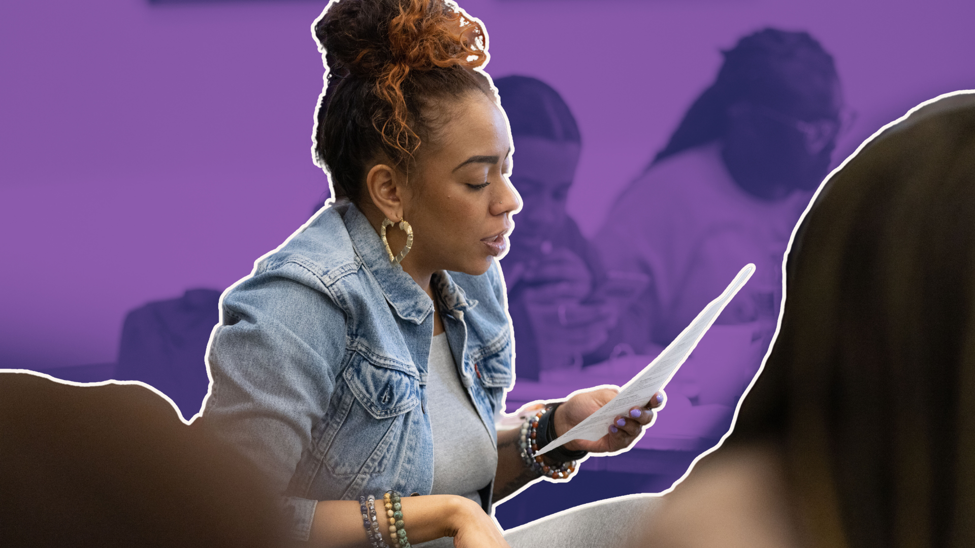 A young woman with curly hair wearing a denim jacket and colorful bracelets, reading a paper at a table in a purple-lit room, with other people in the background.