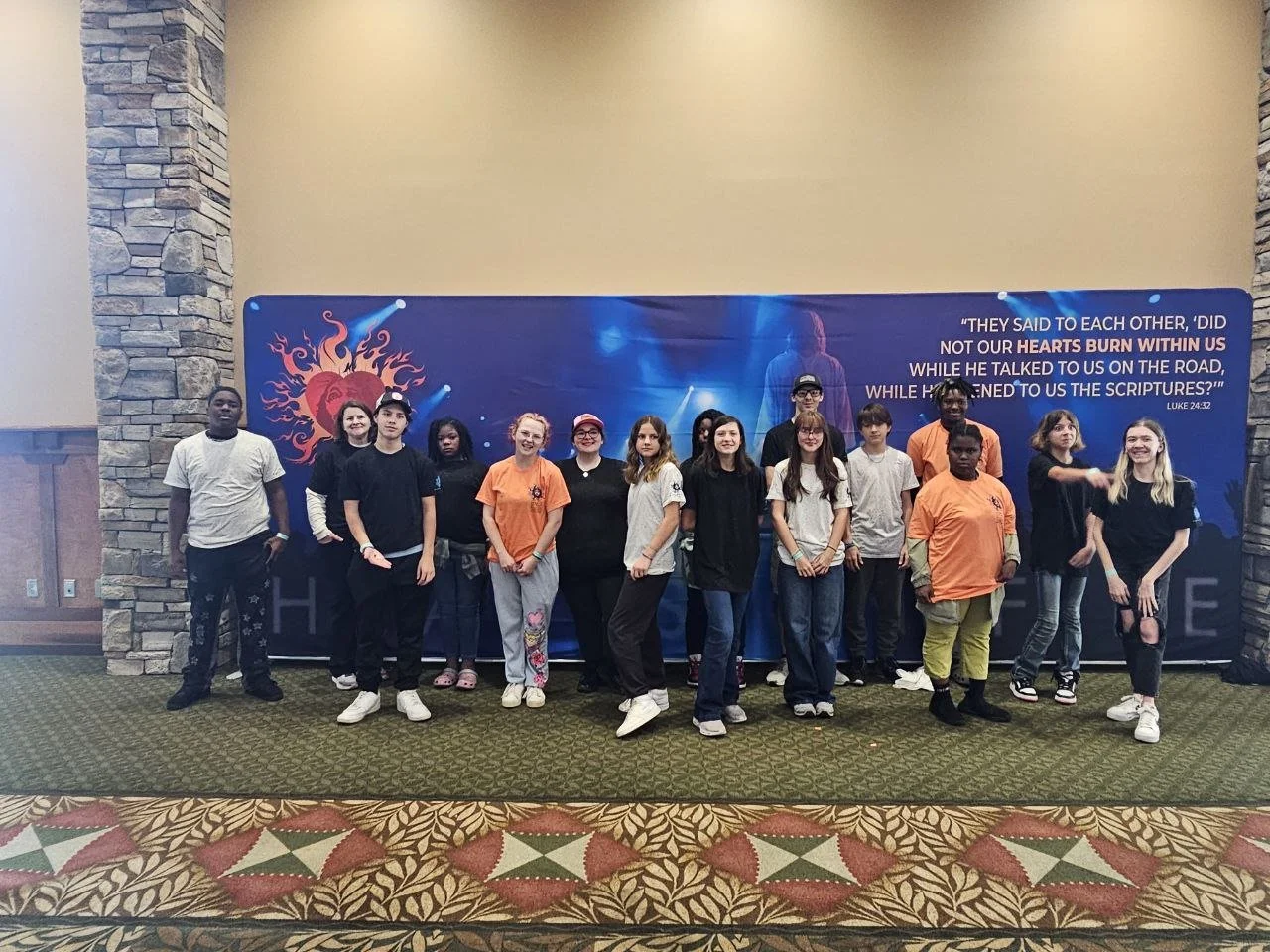 Group of young people posing for a photo in front of a large blue banner with religious text and imagery.