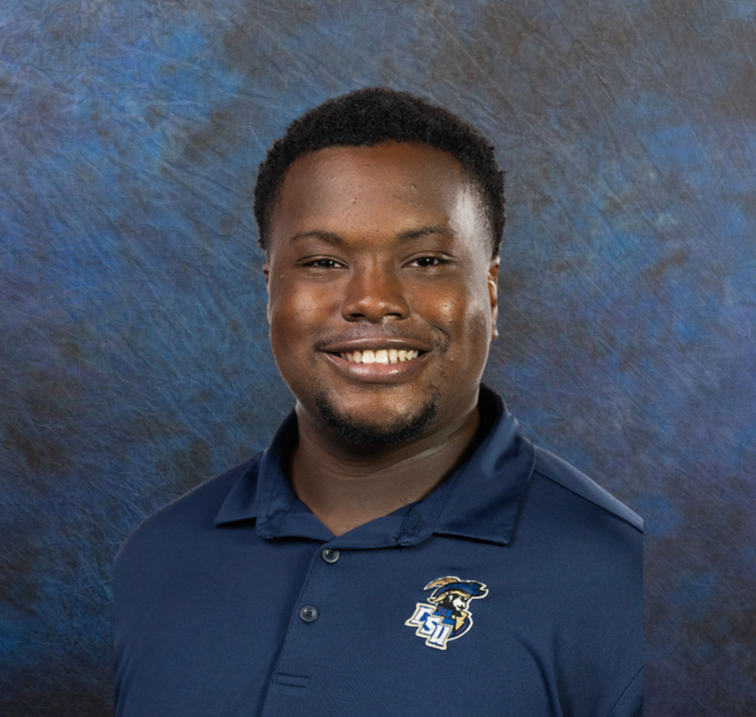 Portrait of a smiling man wearing a navy blue polo shirt with the Louisiana State University logo against a textured blue and brown background.